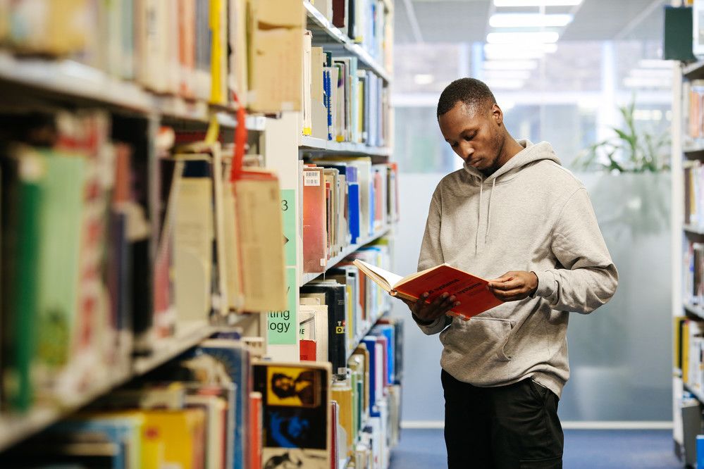 Black man reading a publication among library shelves