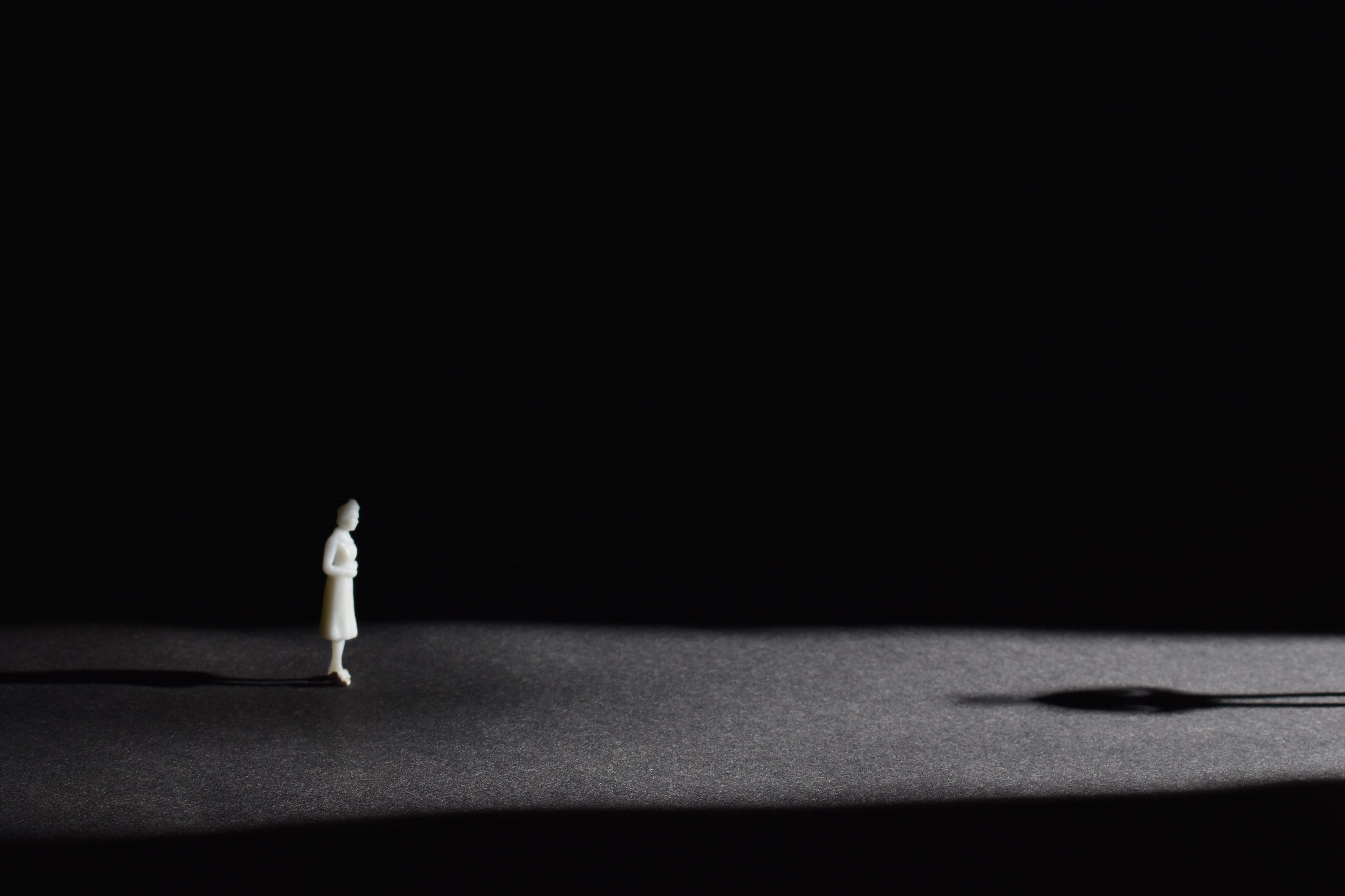 a small white figurine bathed in light on an all black background with a long shadow stretching out t the right 