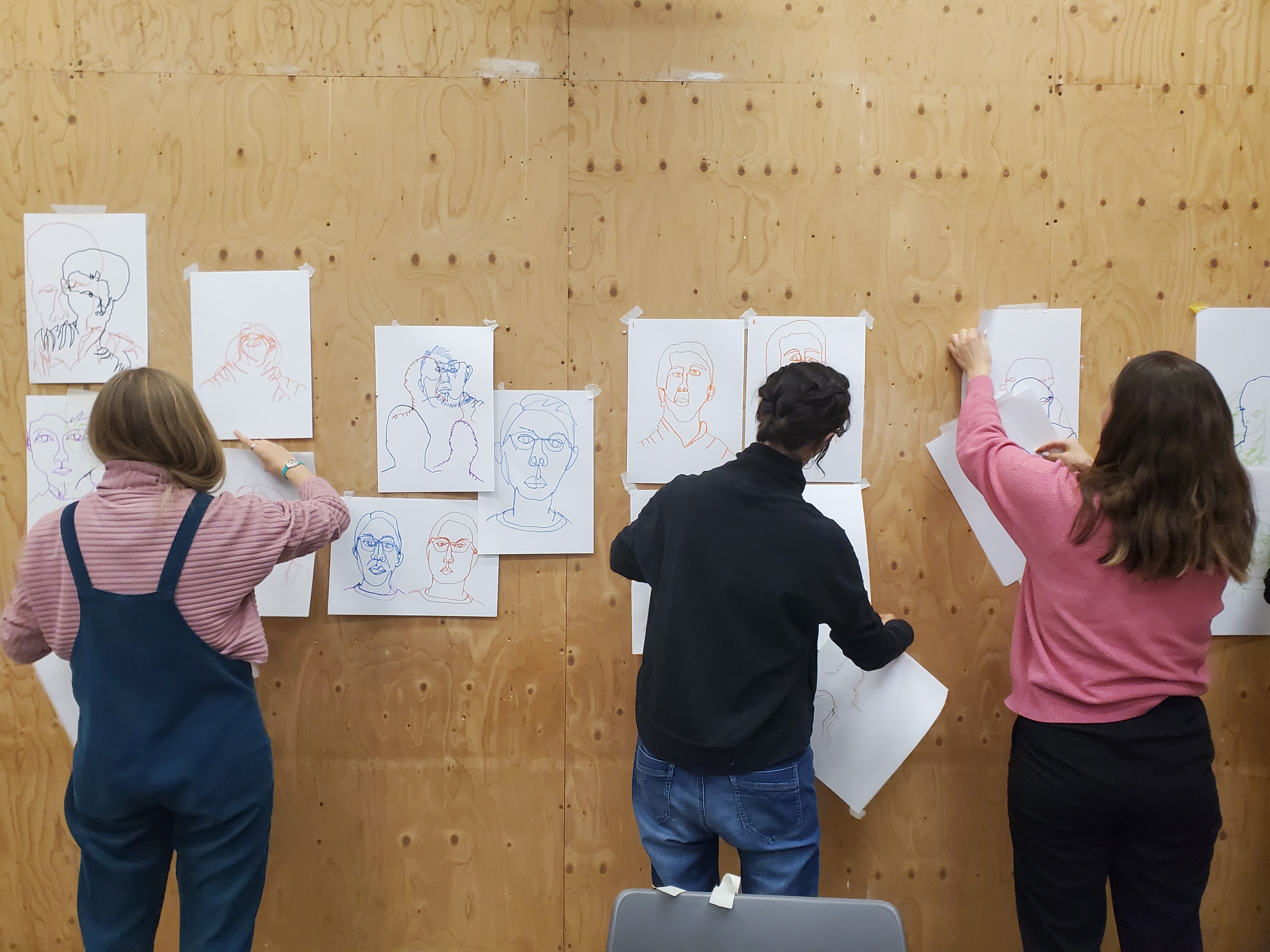 People with their backs to the camera hanging up simple line-drawing portraits on a wall.