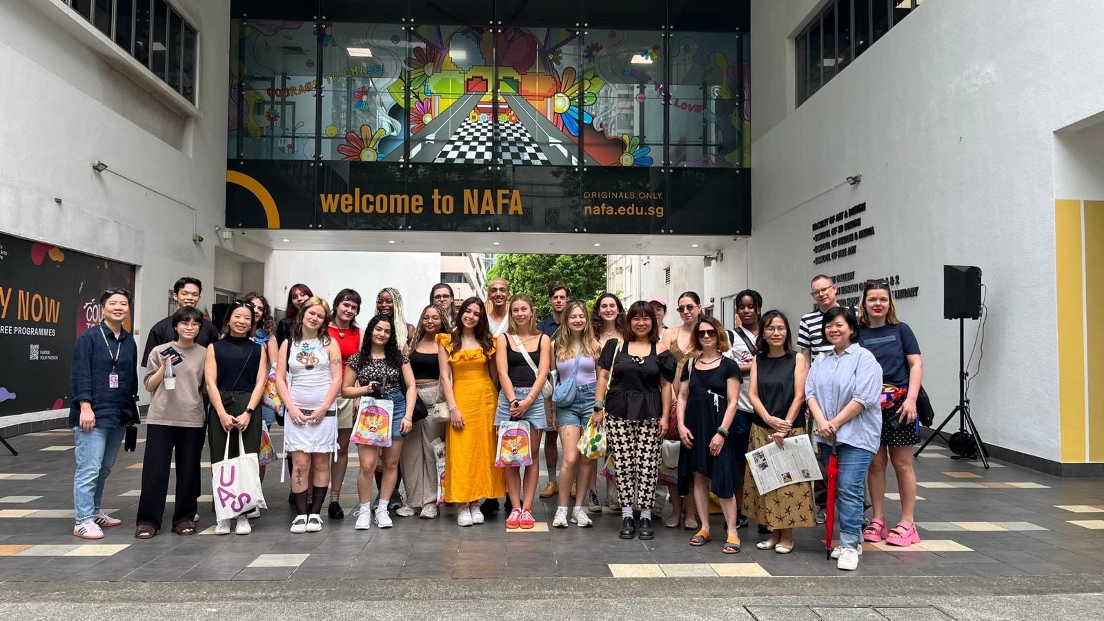 Image shows a group of around 25 people standing in front of a building that reads ‘Welcome to NAFA’ 