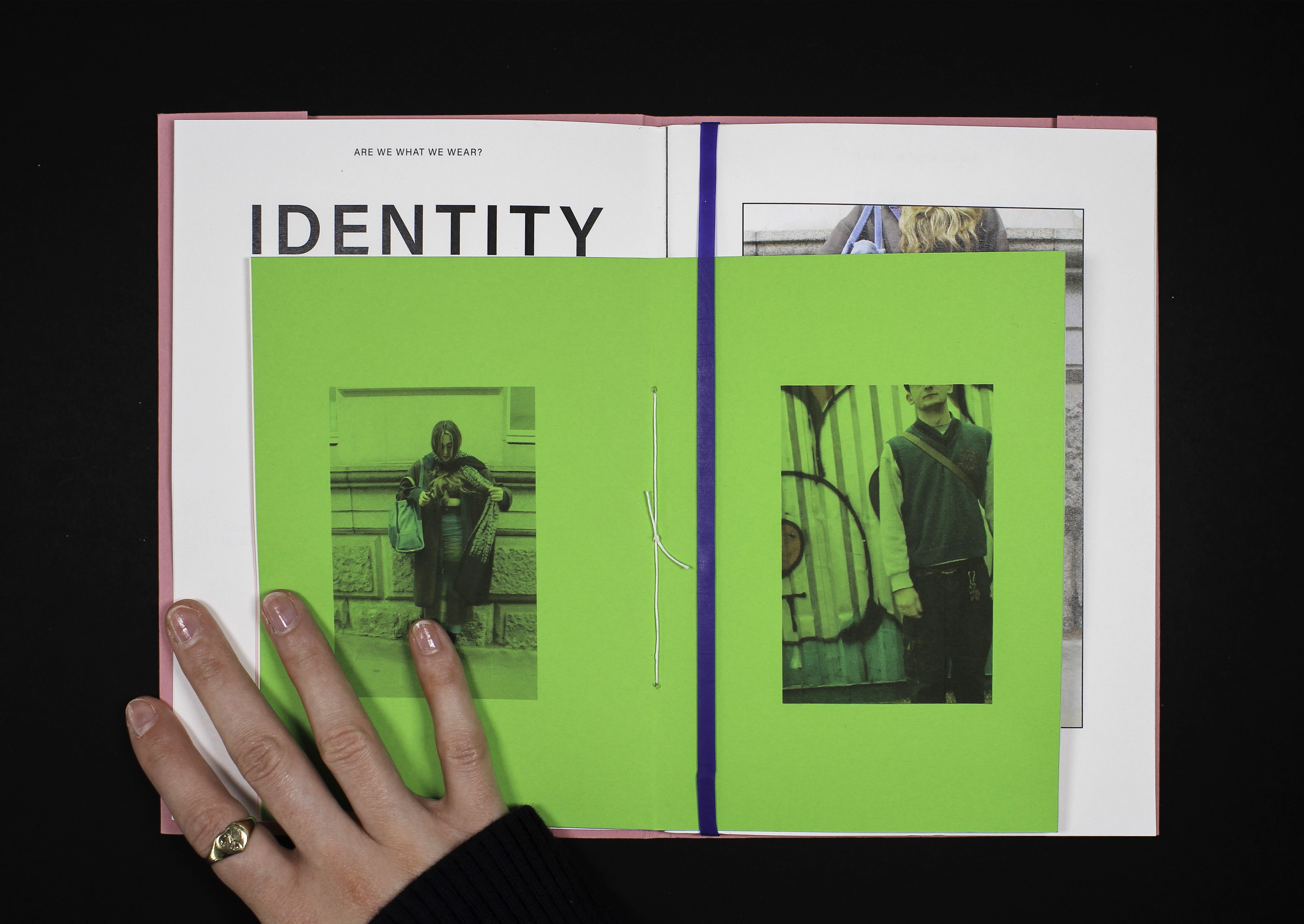 A zine with the word 'identity' is laid out on a table, with a hand turning a page.