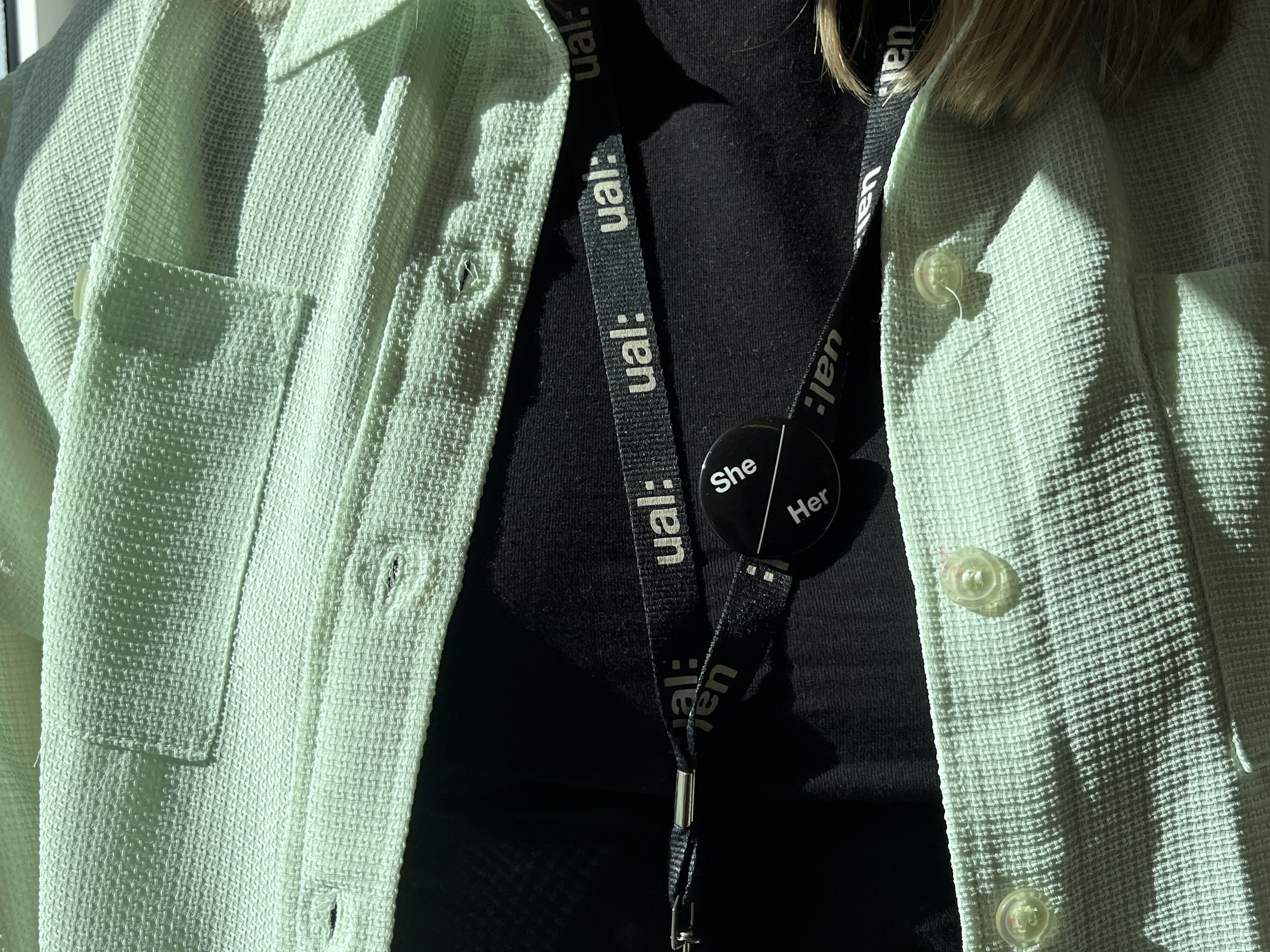 Picture of someone in a light green shirt wearing their lanyard and a pronoun badge attached