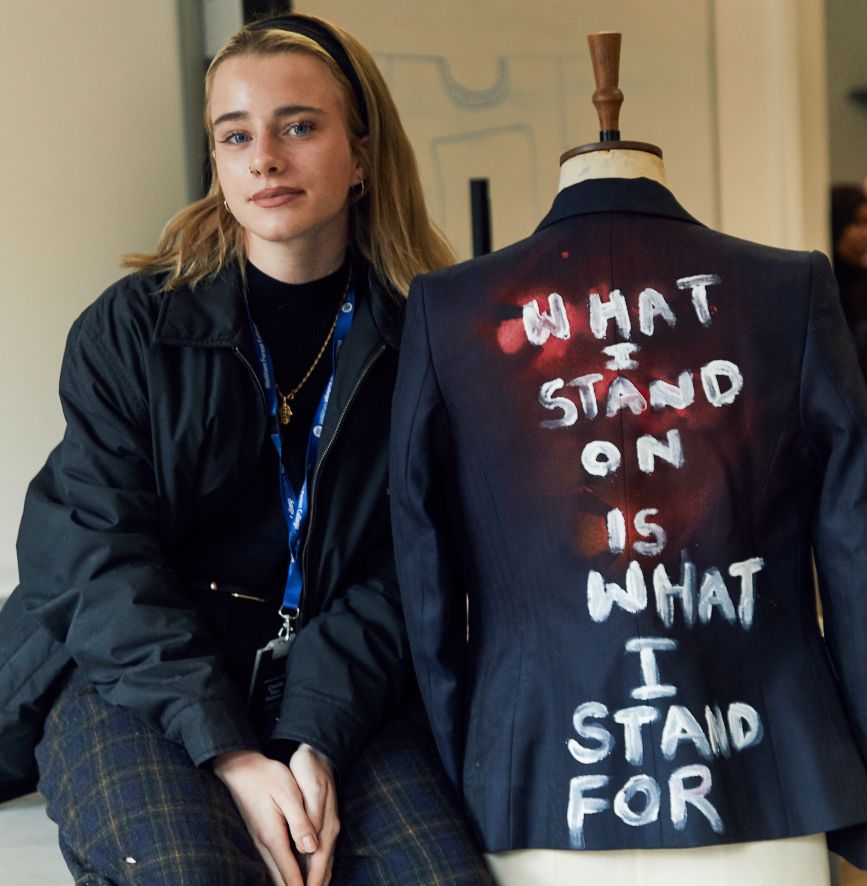 A person sits and smiles next to a jacket that says 
