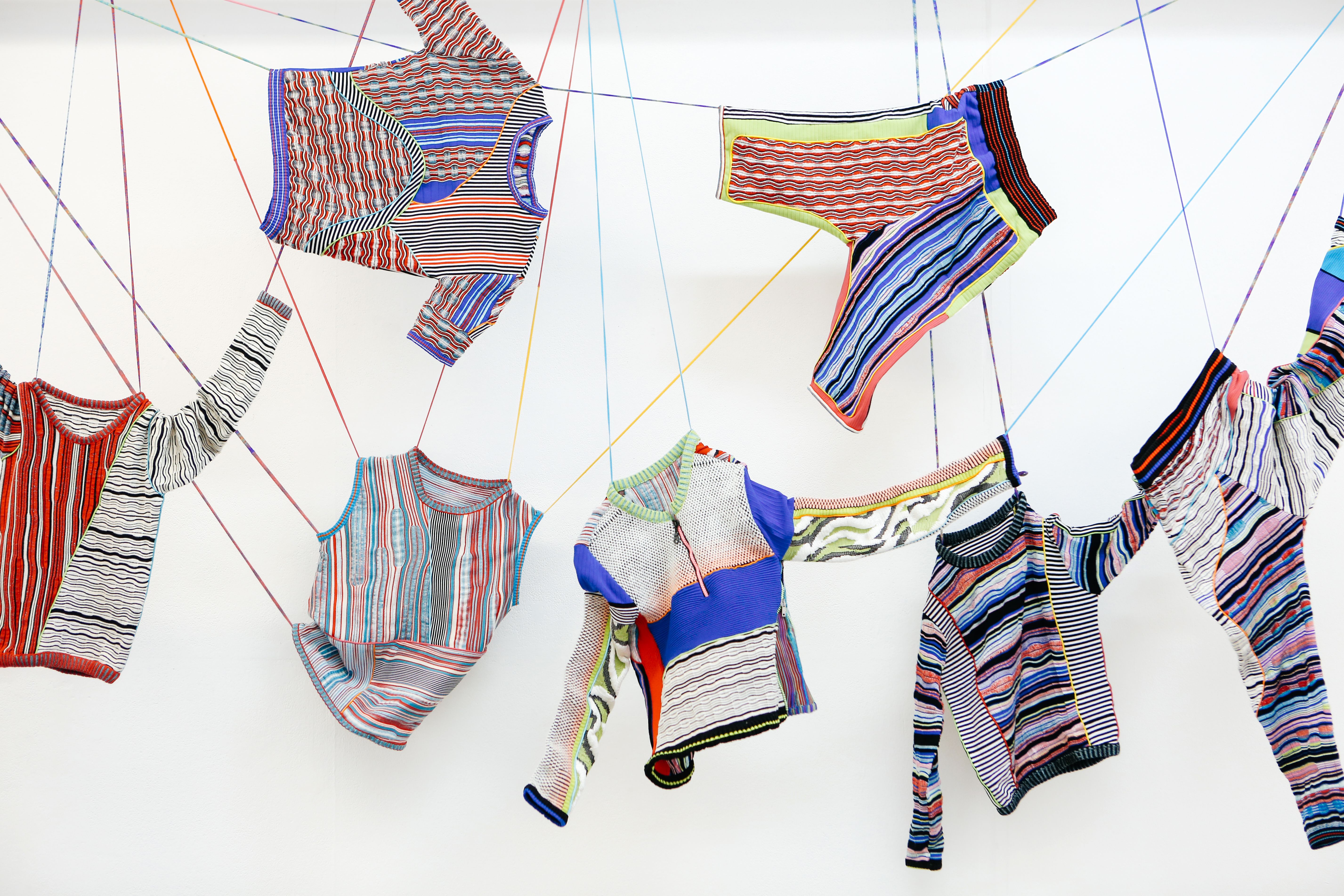Colourful knitted jumpers hang on a web of thread