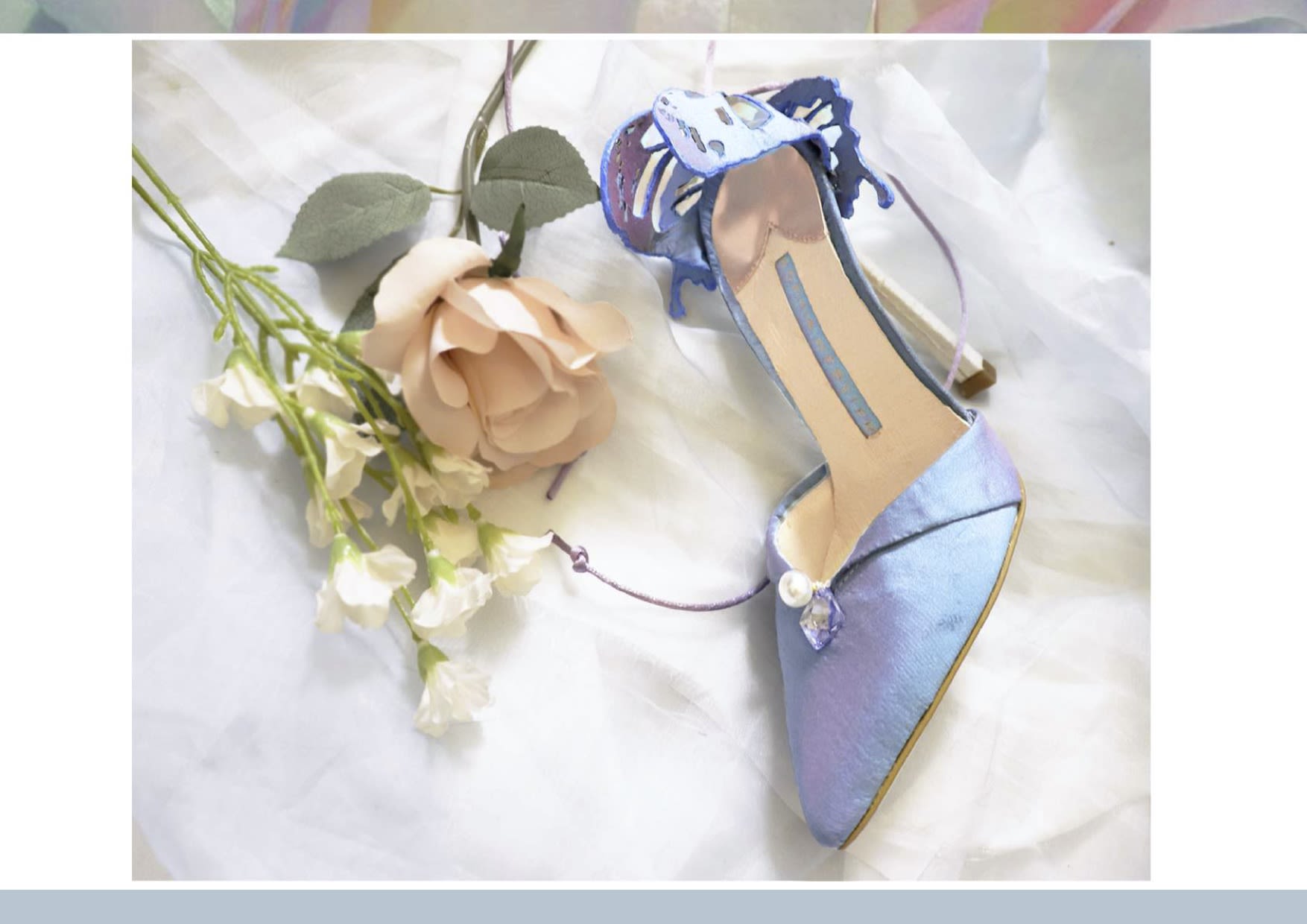 Iridescent blue heeled shoe lying flat on a cream sheet