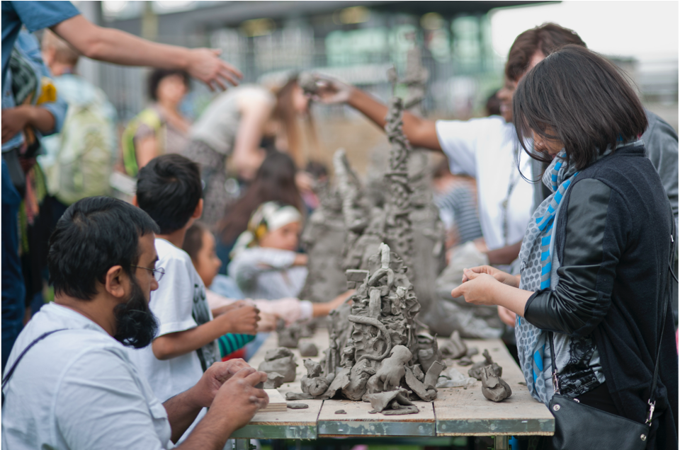 People working and playing with clay on a long public table