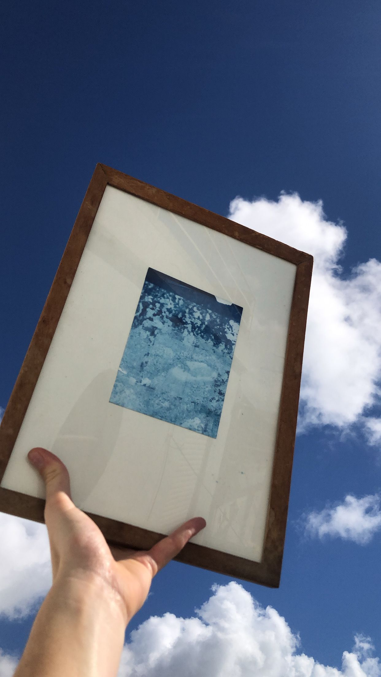 A hand holding a framed image up to the sky