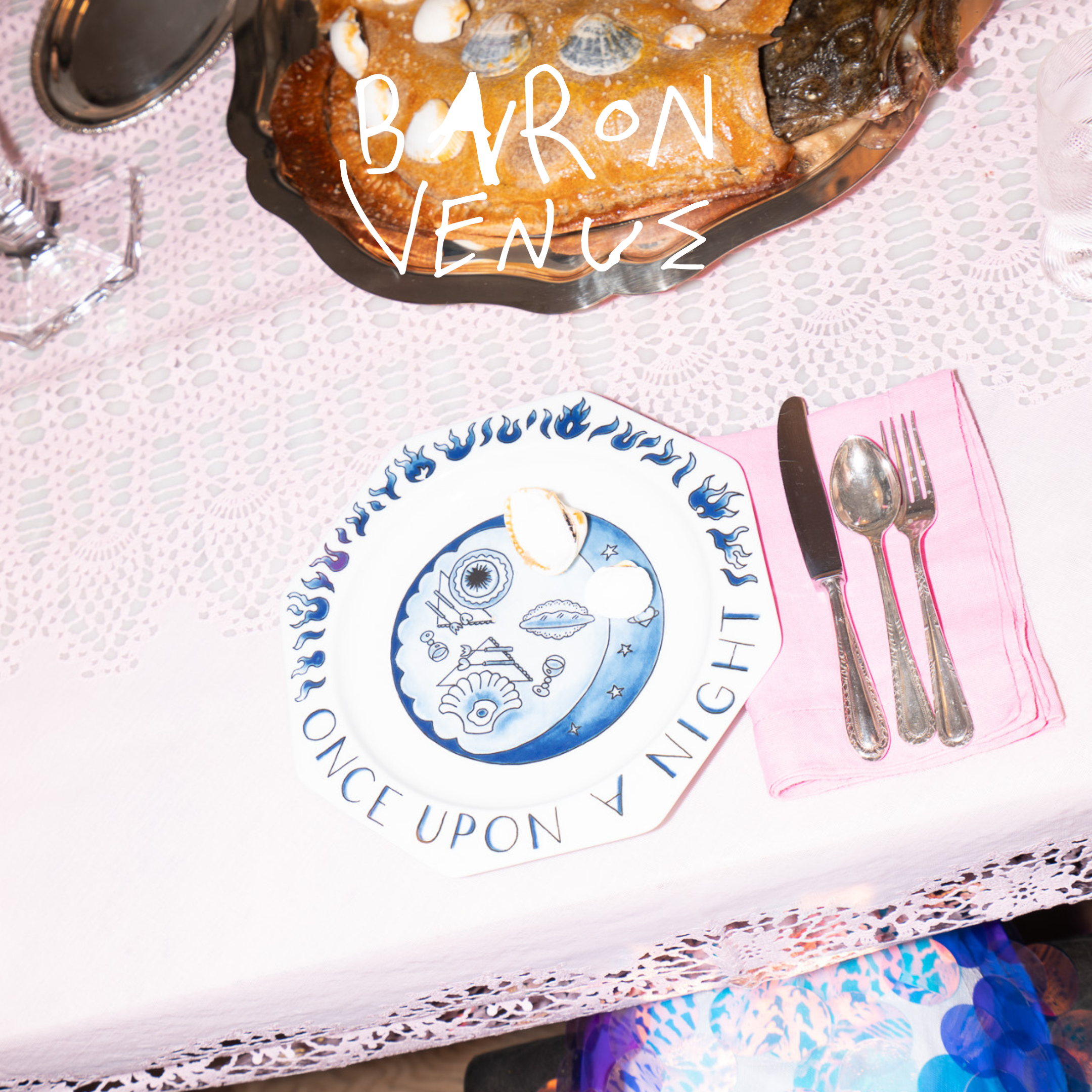 Photo of a table setting with a pink tablecloth a glass, knife and fork. In white, childlike font it says Baron Venus at the top