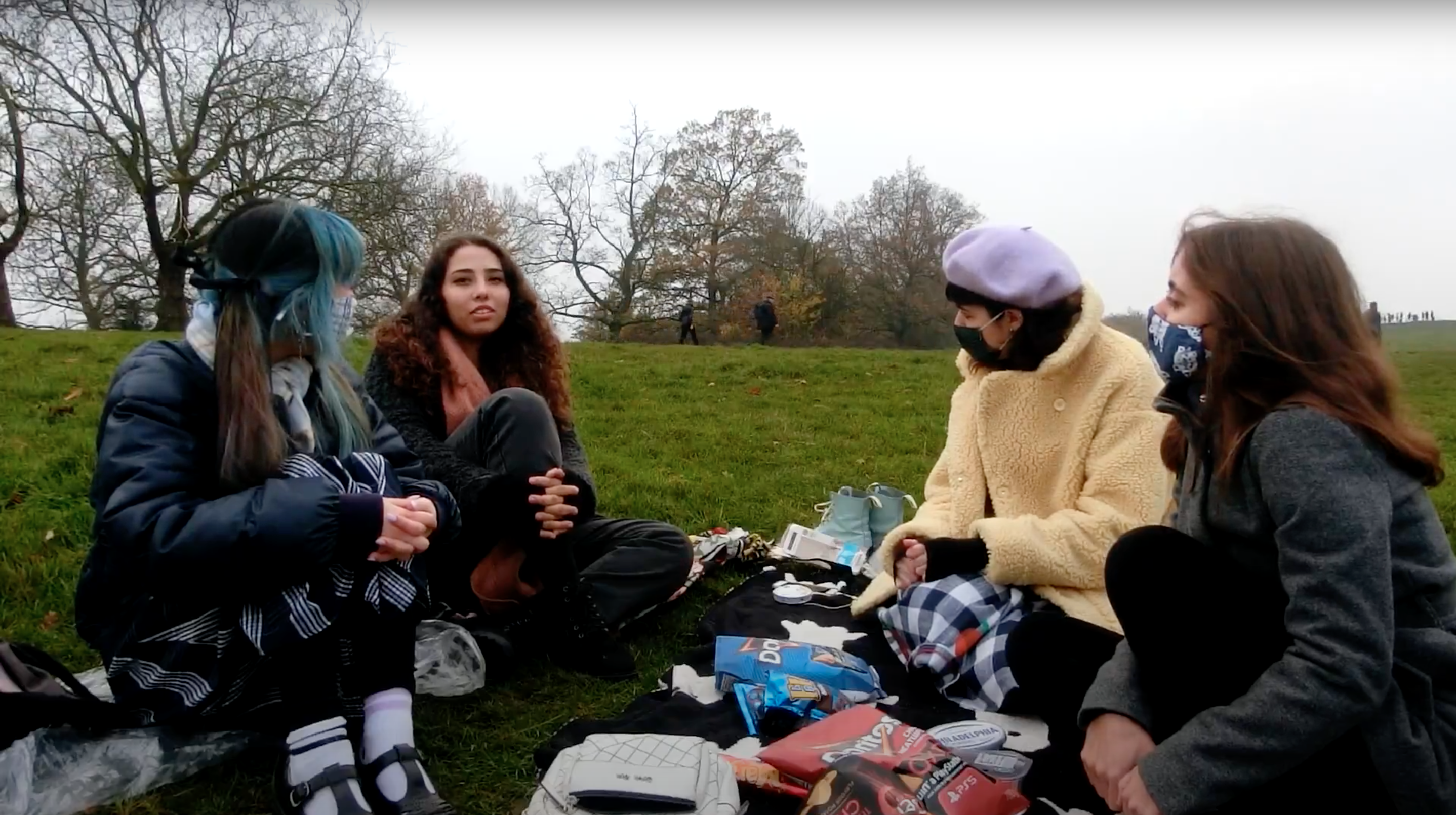women sat in circle in a park wearing face masks