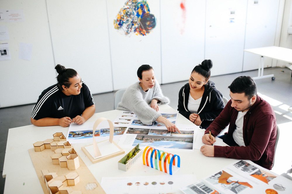 Three students working at a desk with their tutor.
