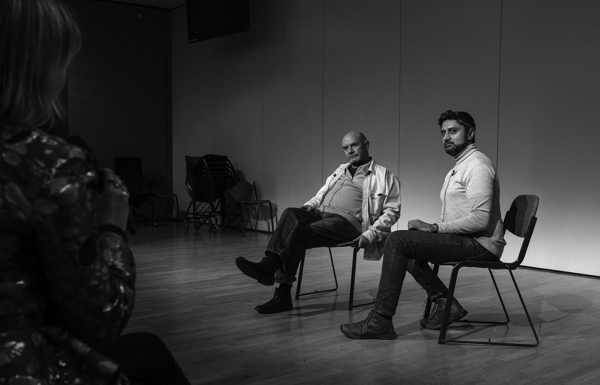 A black and white wide shot of Nick Hornby and Ray Grewal seated and in conversation.