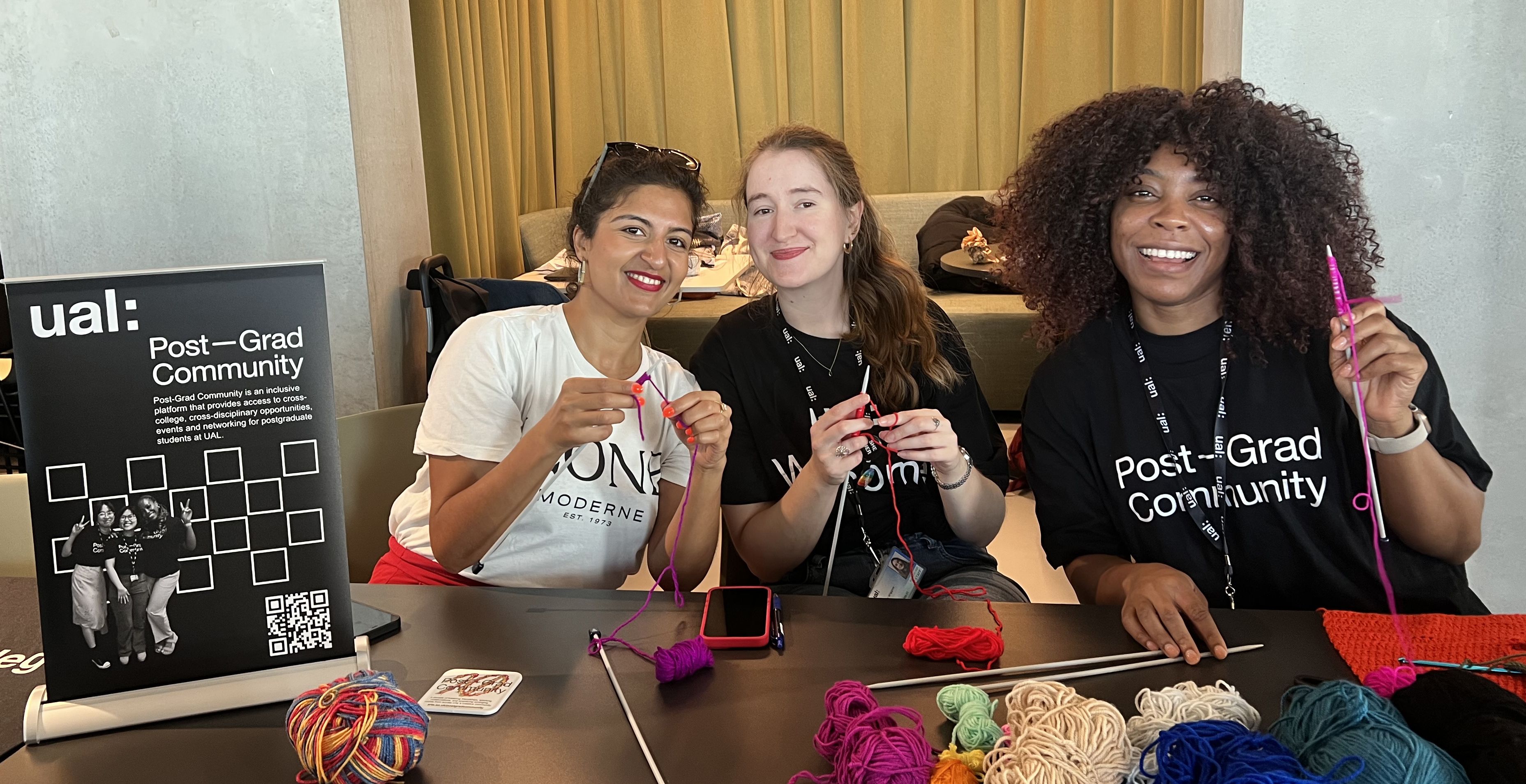 three people smiling with some knitting and post-grad community  banner