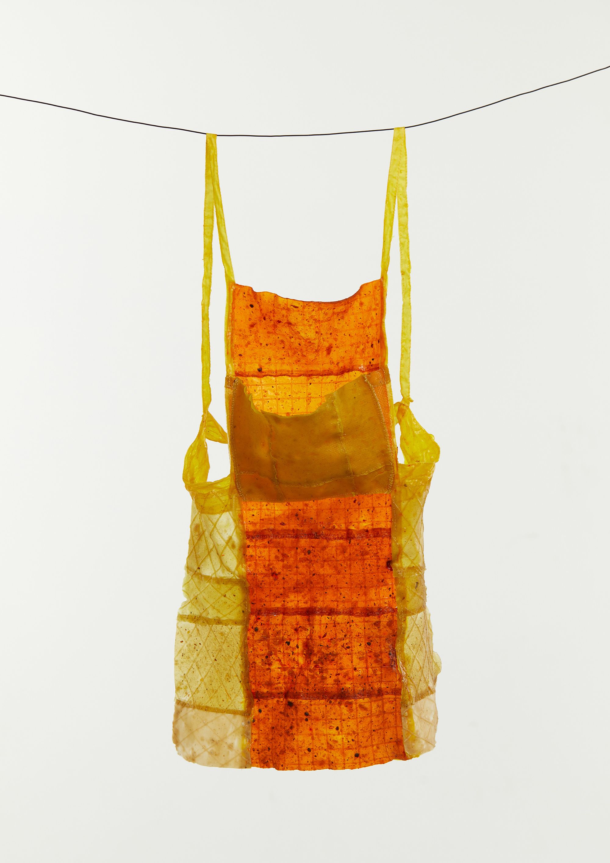 A dress garment from the FATWEAR collection, the dress is created from waste fat liquids which result in a yellow and orange material. The dress is hanging from a wire. 
