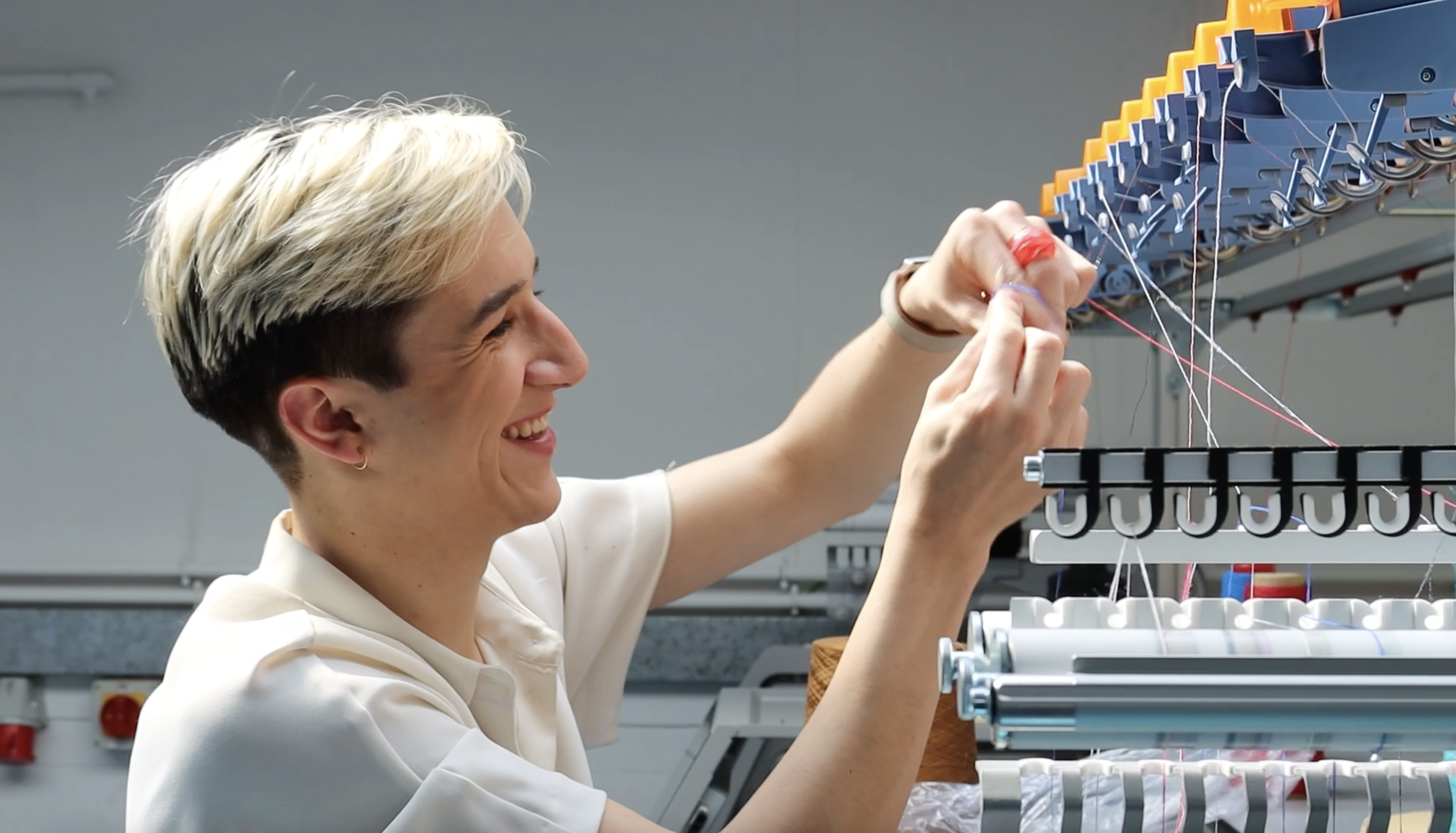A picture of someone threading a knitting machine while smiling