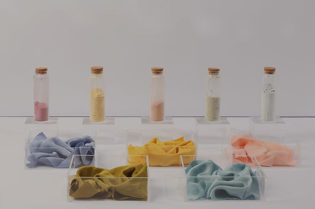 Five vials of natural dye are in the background with five samples of the colours they produce on fabric in the foreground