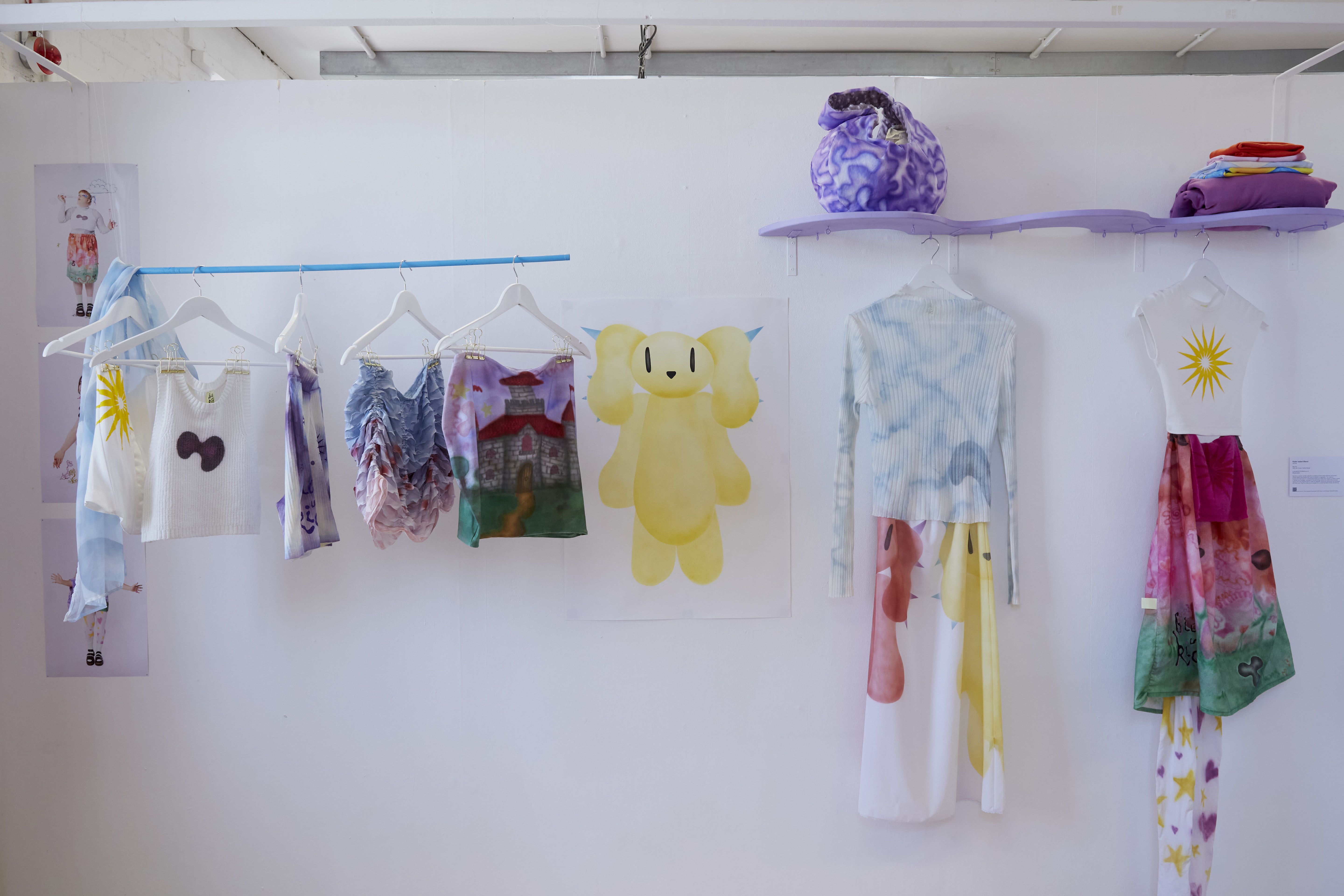 Image shows a series of pastel coloured items of clothing hanging against a white wall.