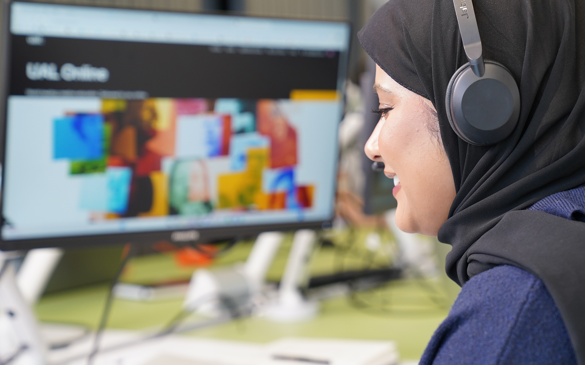 A woman working with black headphones looking at computer screen