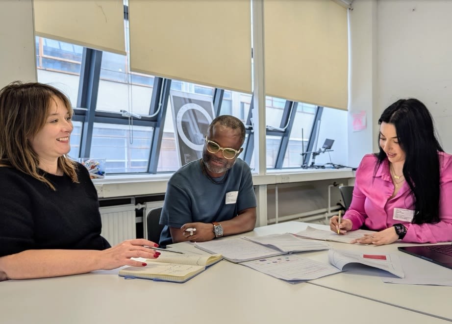 Three people sit around a table talking. 
