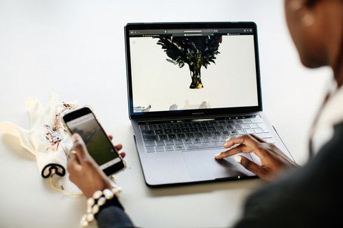 The back of a person's head and hand just visible in the foreground. They are working on a Macbook and a phone and there is a design visible on screen