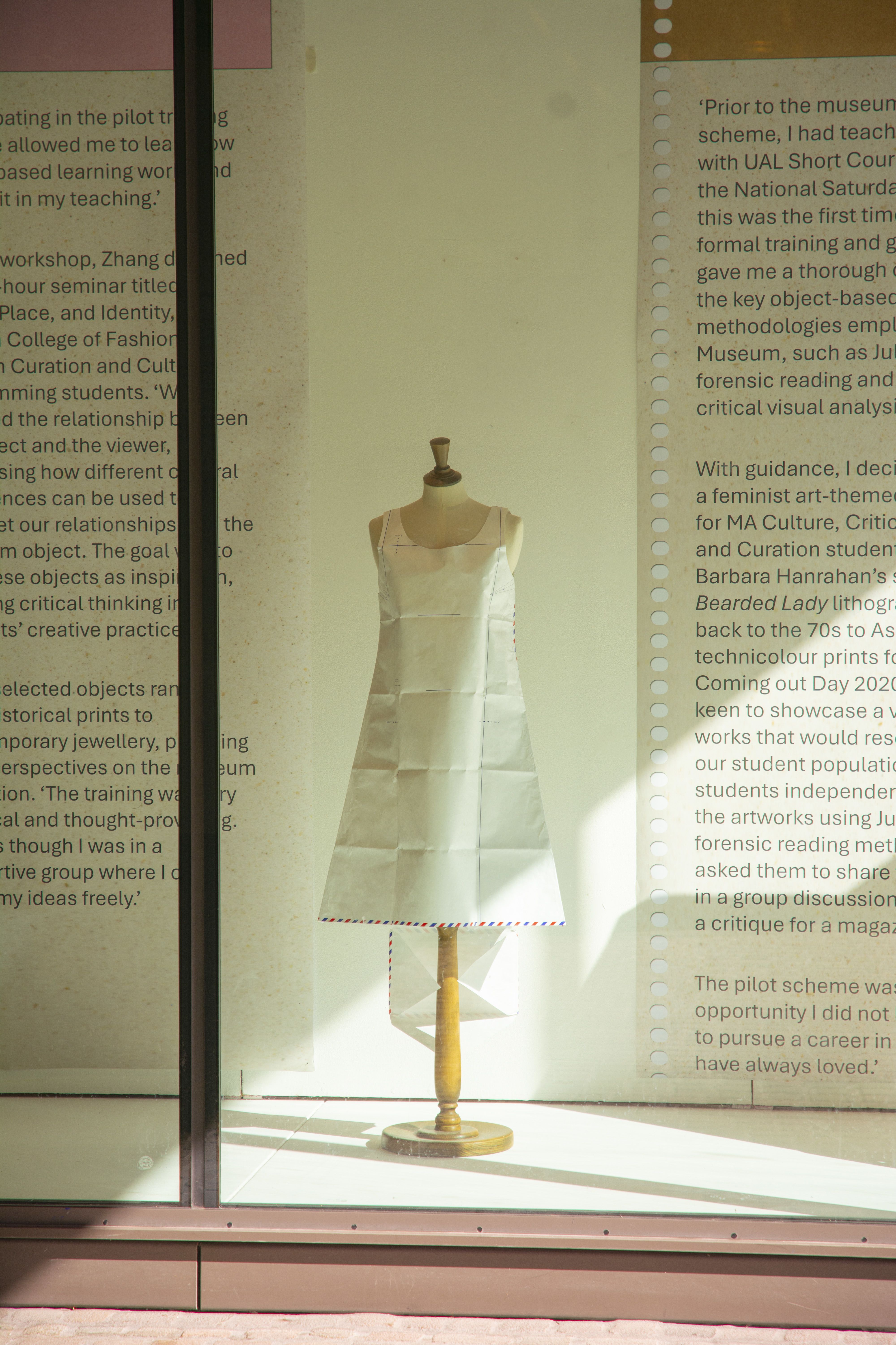 Paper dress exhibited behind glass in a window exhibition.