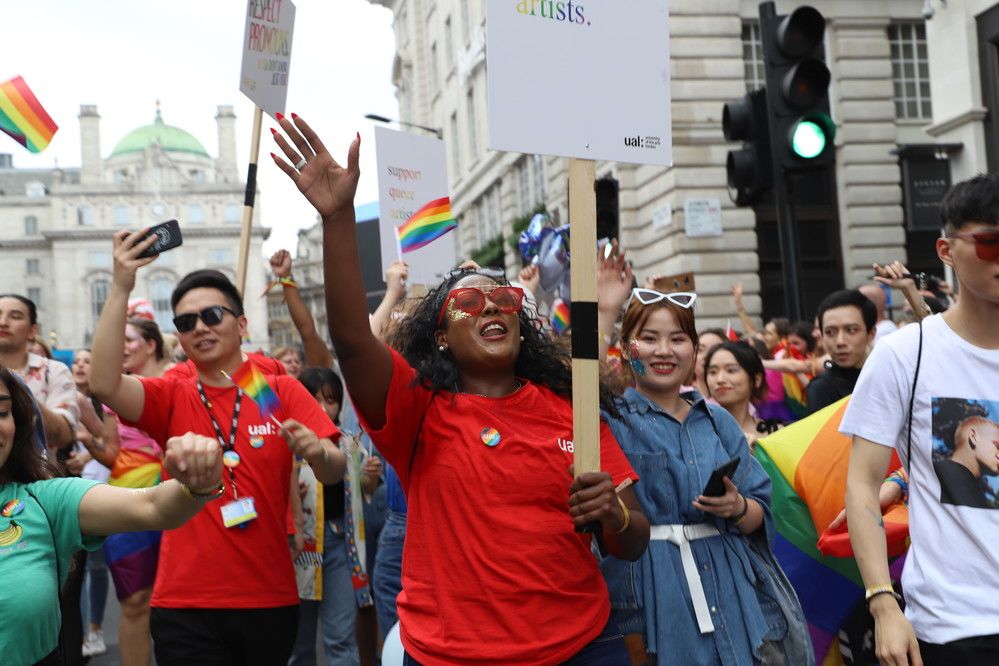 UAL LGBTQ+ protesters at Pride in London marching and celebrating with one black protester holding a sign and hand in the air