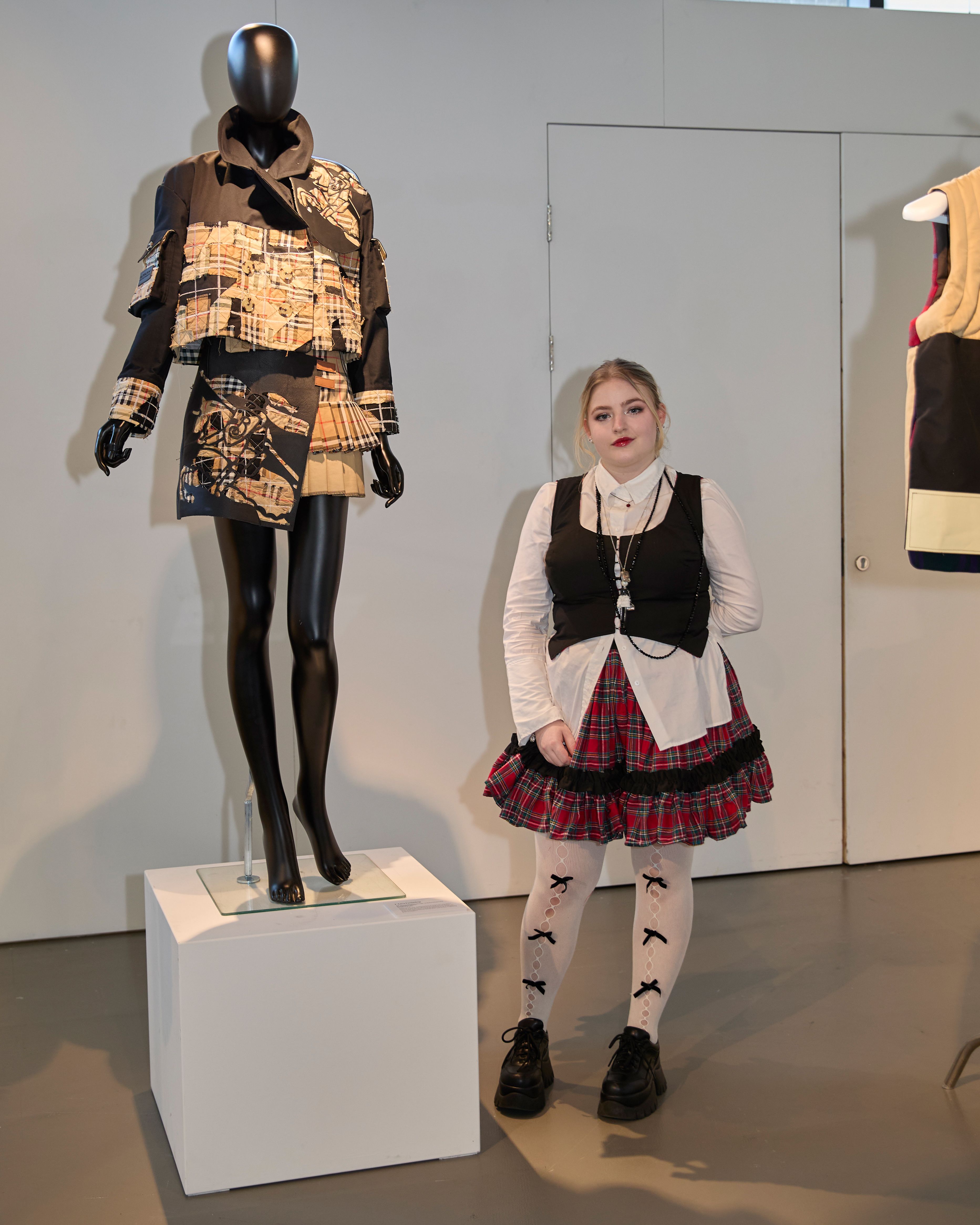 Person smiling at camera, standing next to mannequin with blazer and skirt on.