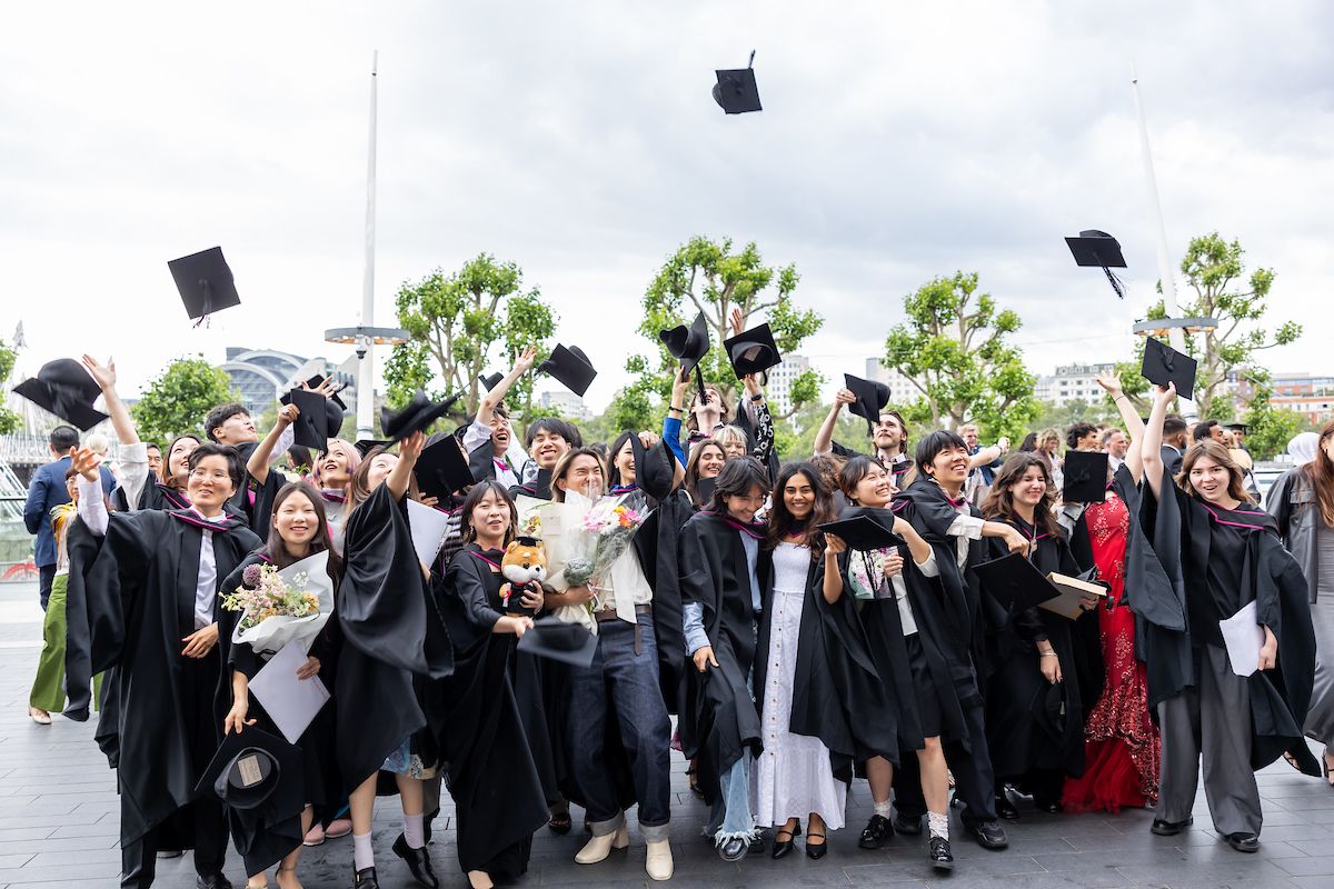 a group of graduate students celebrating and throwing their hats in the air