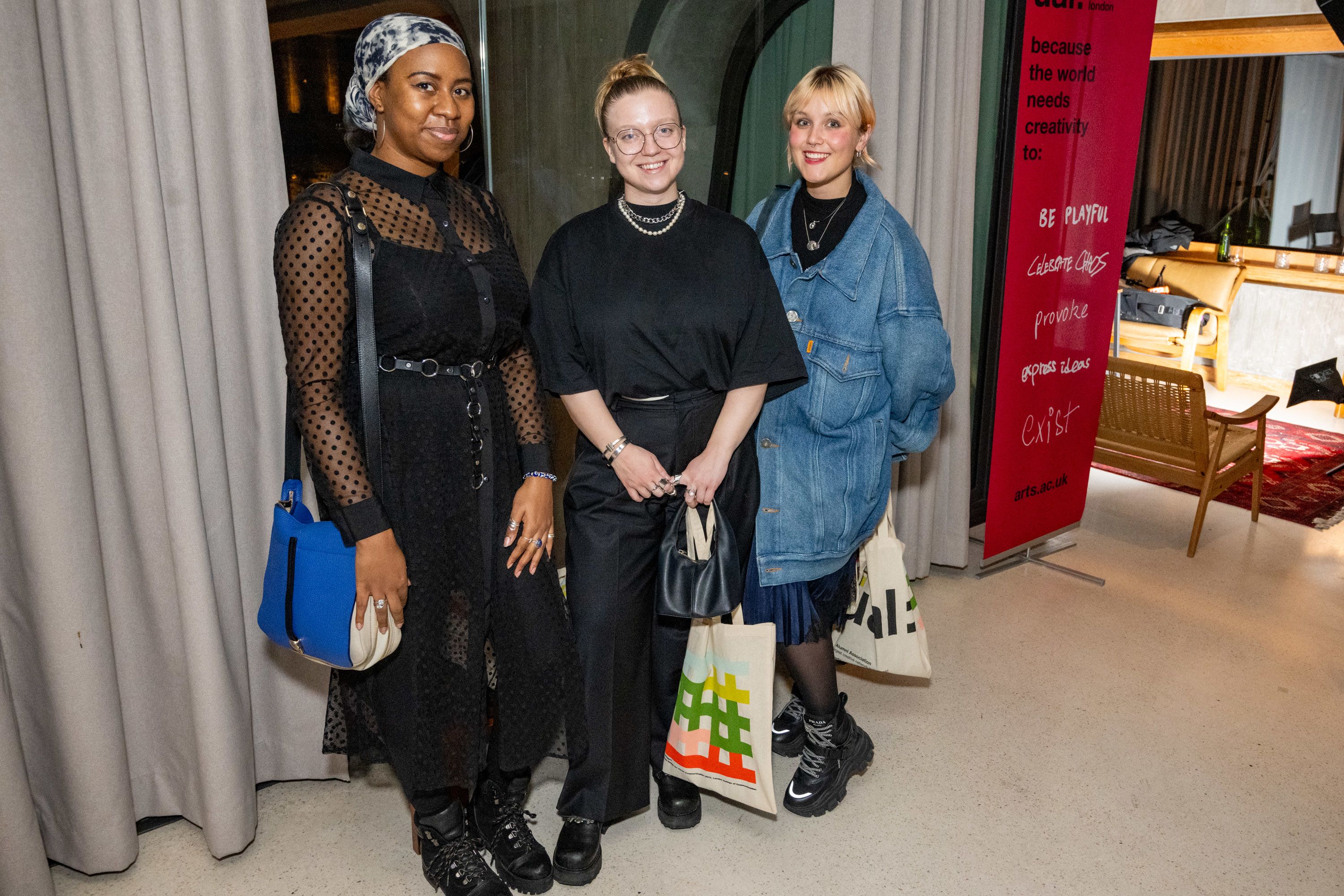 Three guests at the reception; holding UAL alumni tote bags and smiling to the camera