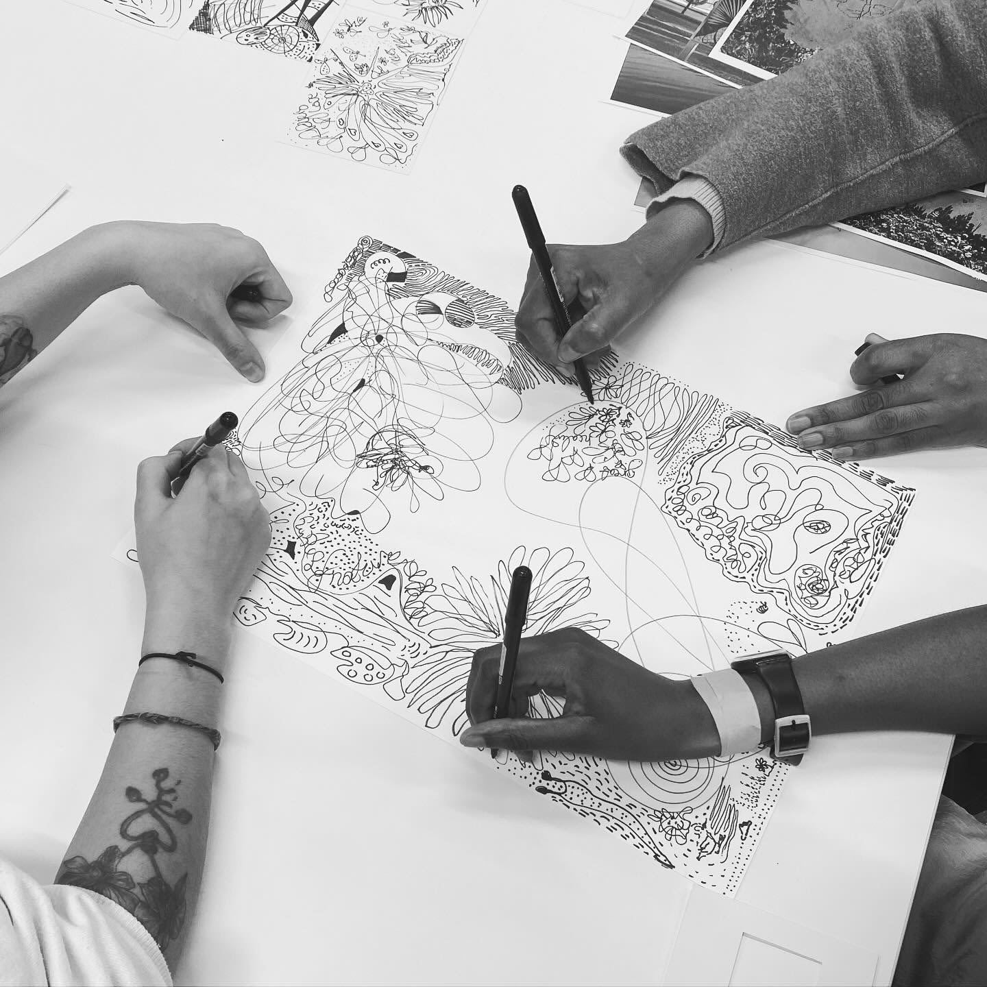Three hands on a table, drawing patterns on sheet