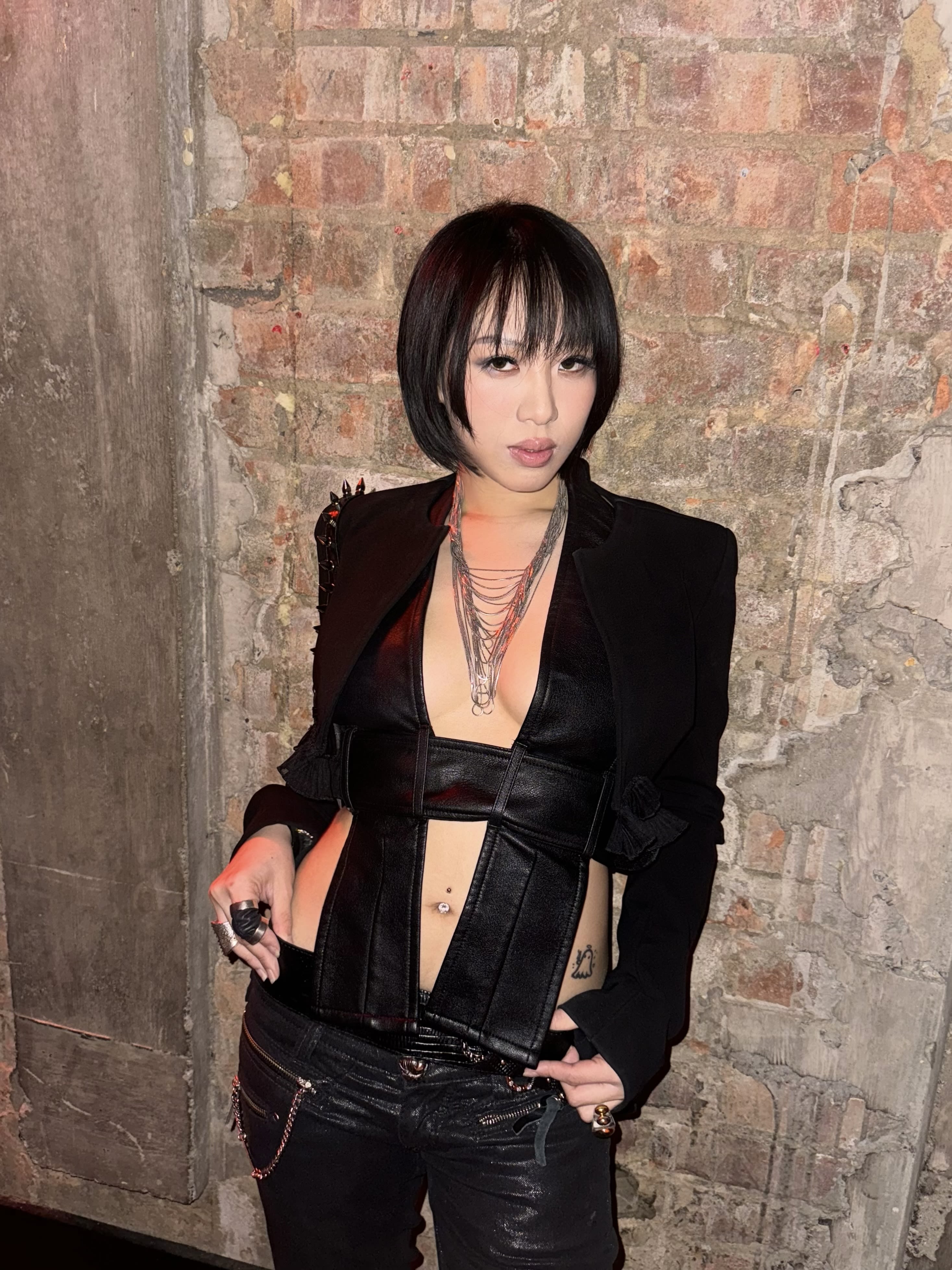 Lancy Liu, standing in front of a concrete wall, wearing a black suit blazer and crop top