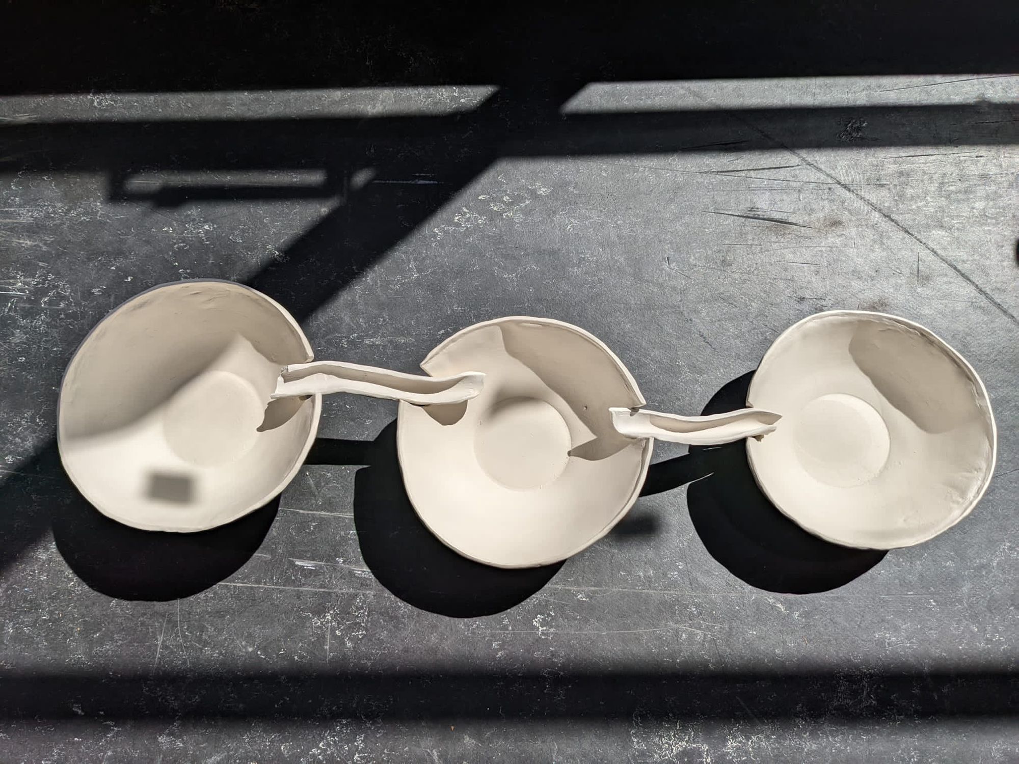 3 small bowls are interlinked with small creviced links. The image is a birds-eye view and sees them partially illuminated by slanting daylight.