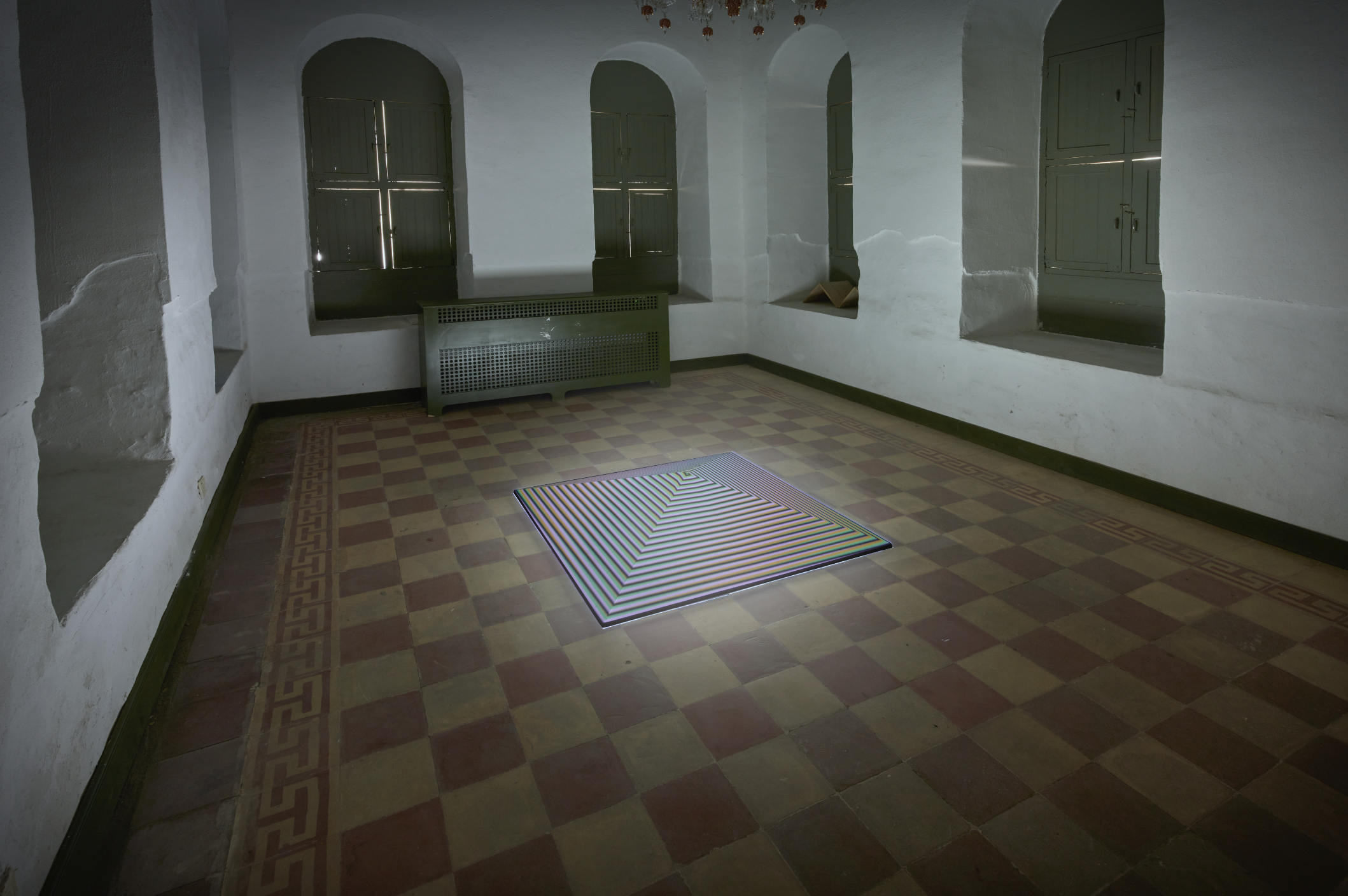 A low pyramid sculpture in the middle of room. The windows around the outside are all shuttered. 