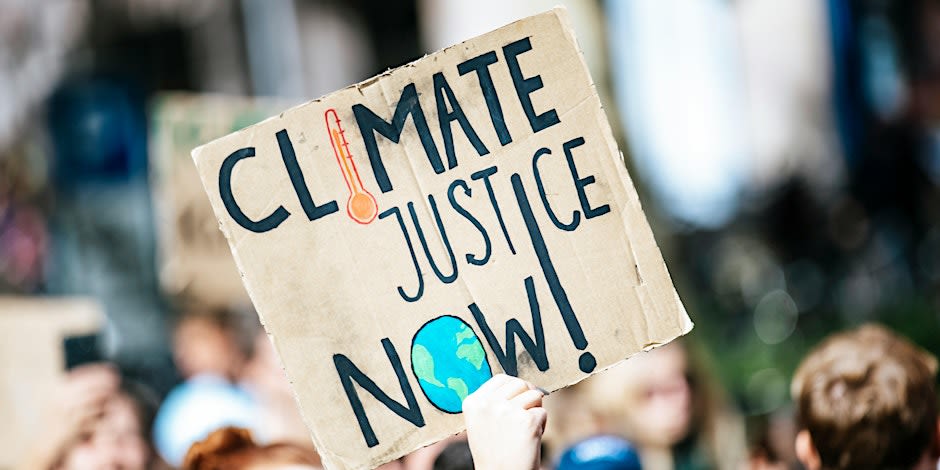 Person holding up cardboard sign, which reads 'Climate Justice Now!' on.