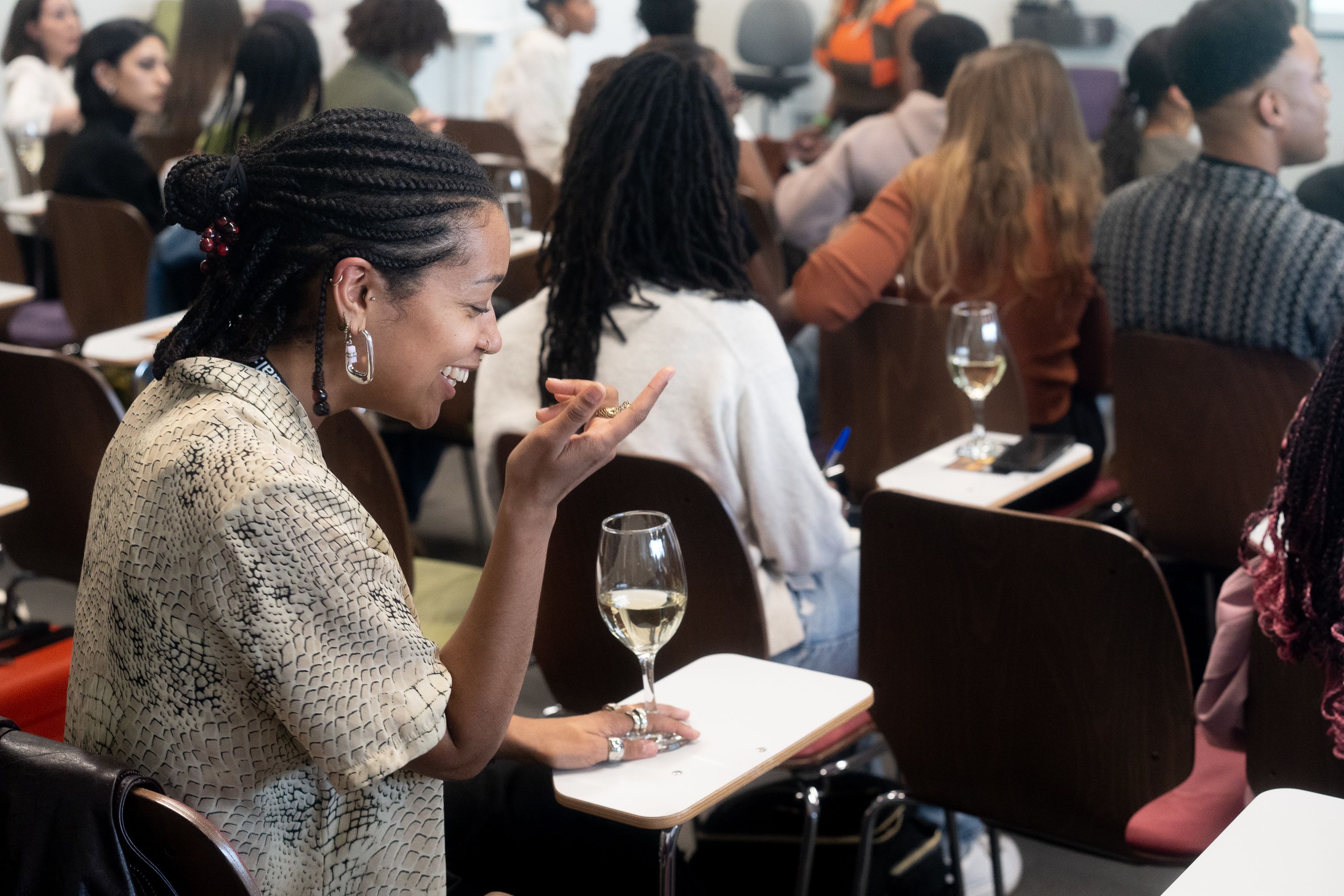 A smiling attendee holds a glass of wine while chatting at a seated social event.