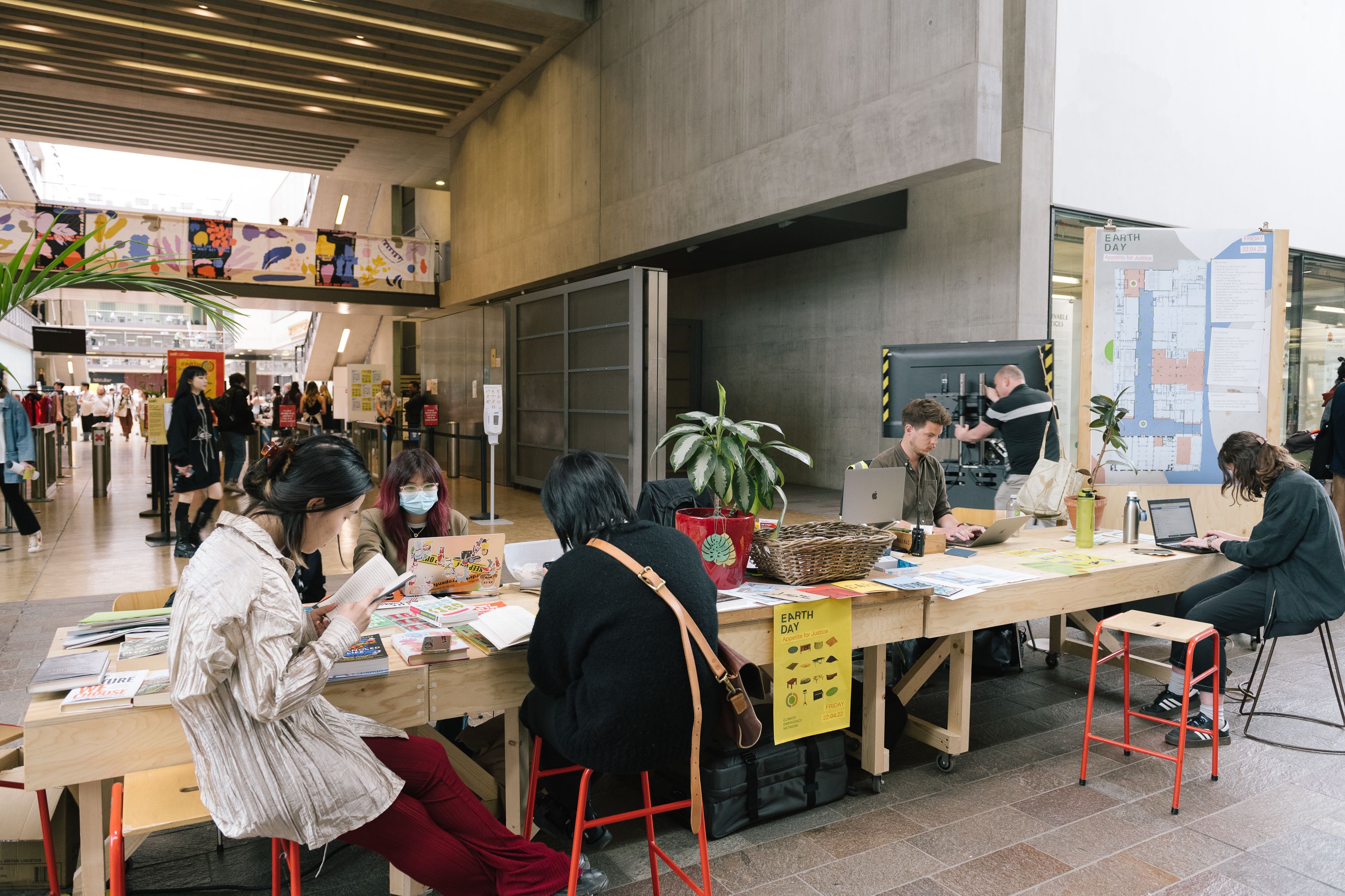 A group of people working at a table at CSM. They are making and doing and plants and banners are visible.