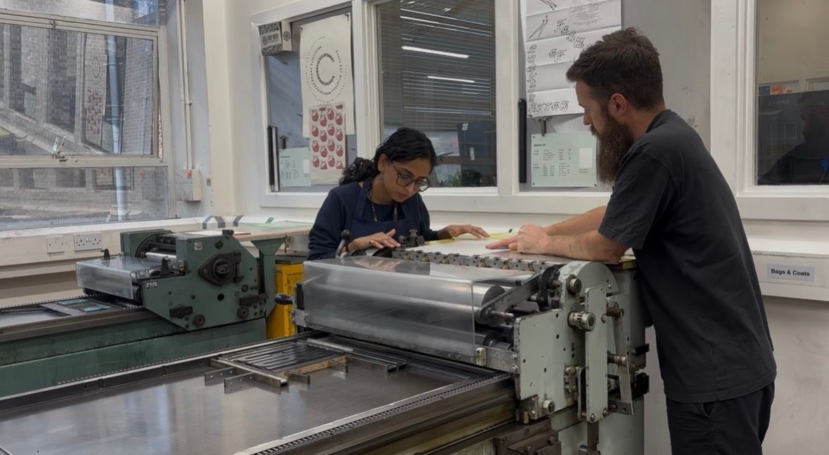 An Indian, female student collaborates with a white male peer in the printmaking studios.