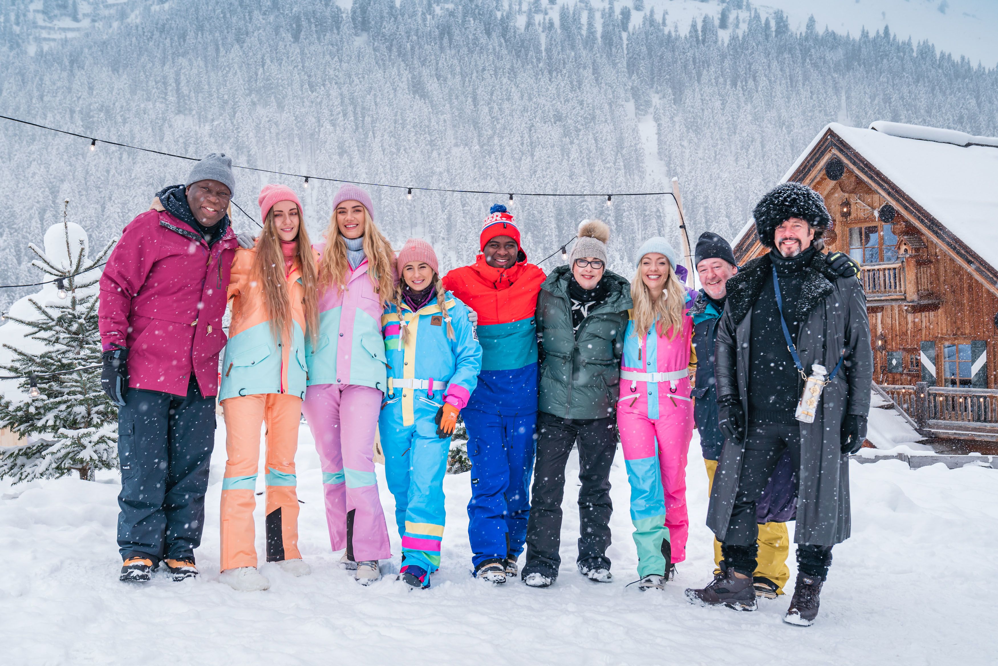 A group of 9 people dressed in warm snowsuits standing in a line in a snowy landscape.