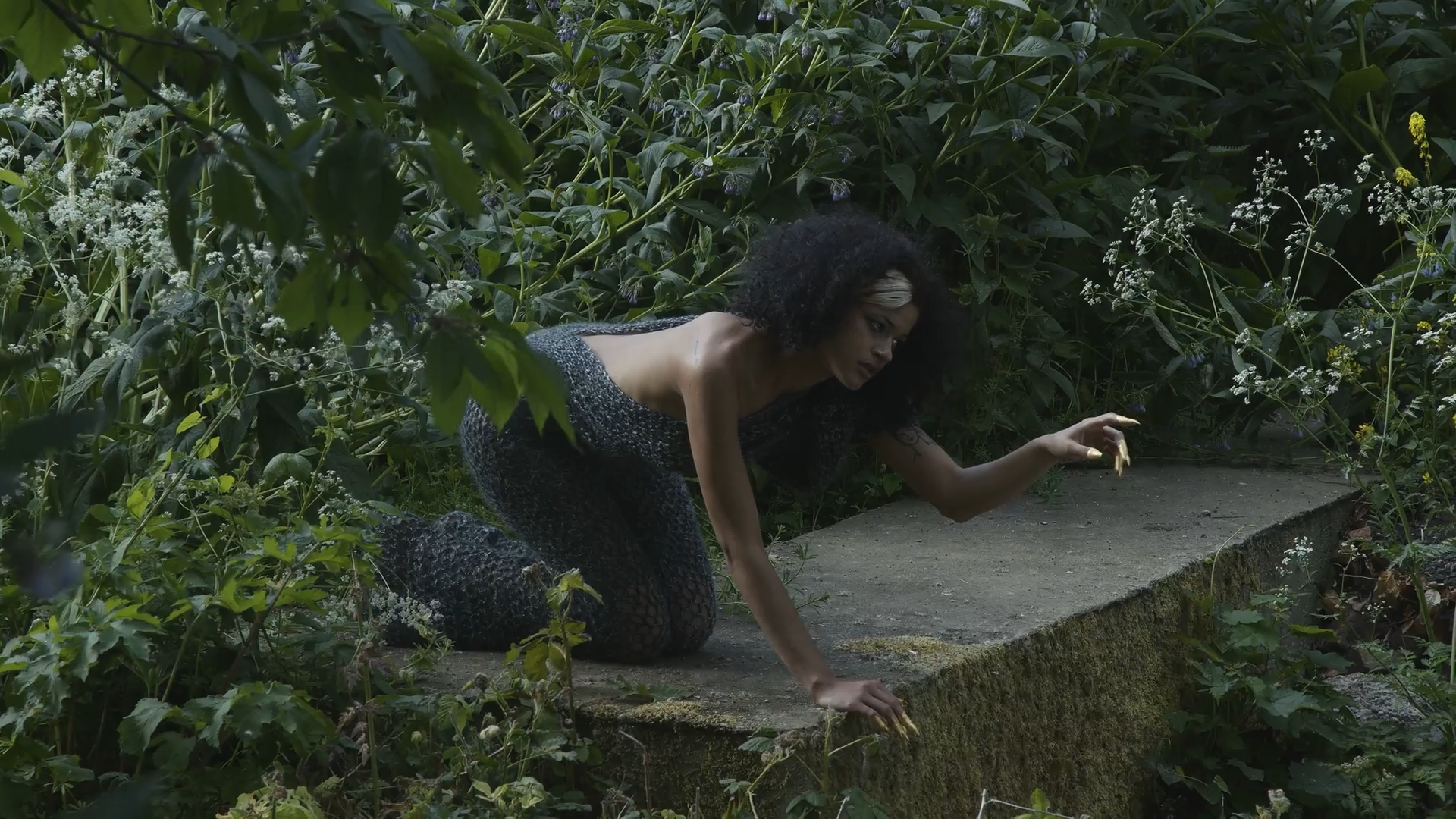 A women crawling on the ground in a bed of green leaves.