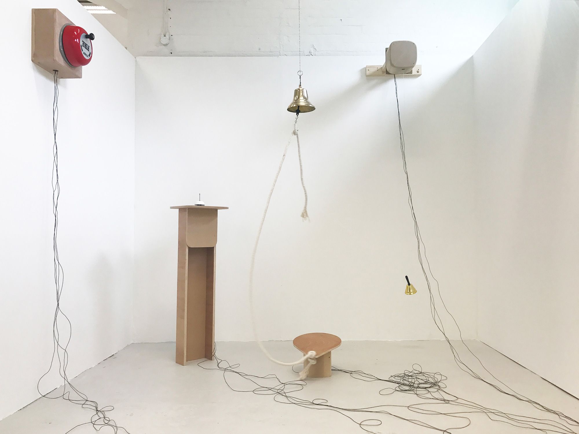 Degree Show 2017 installation, a selection of different type of bells attached to the white wall or presented on a plinth. Wires are connected to each bell.