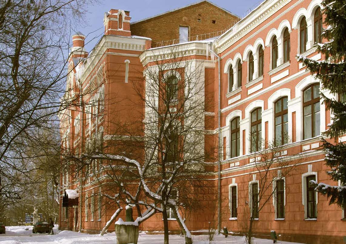 A large redbrick building, in the foreground is snow covered trees. Snow is on the ground and the top of the building