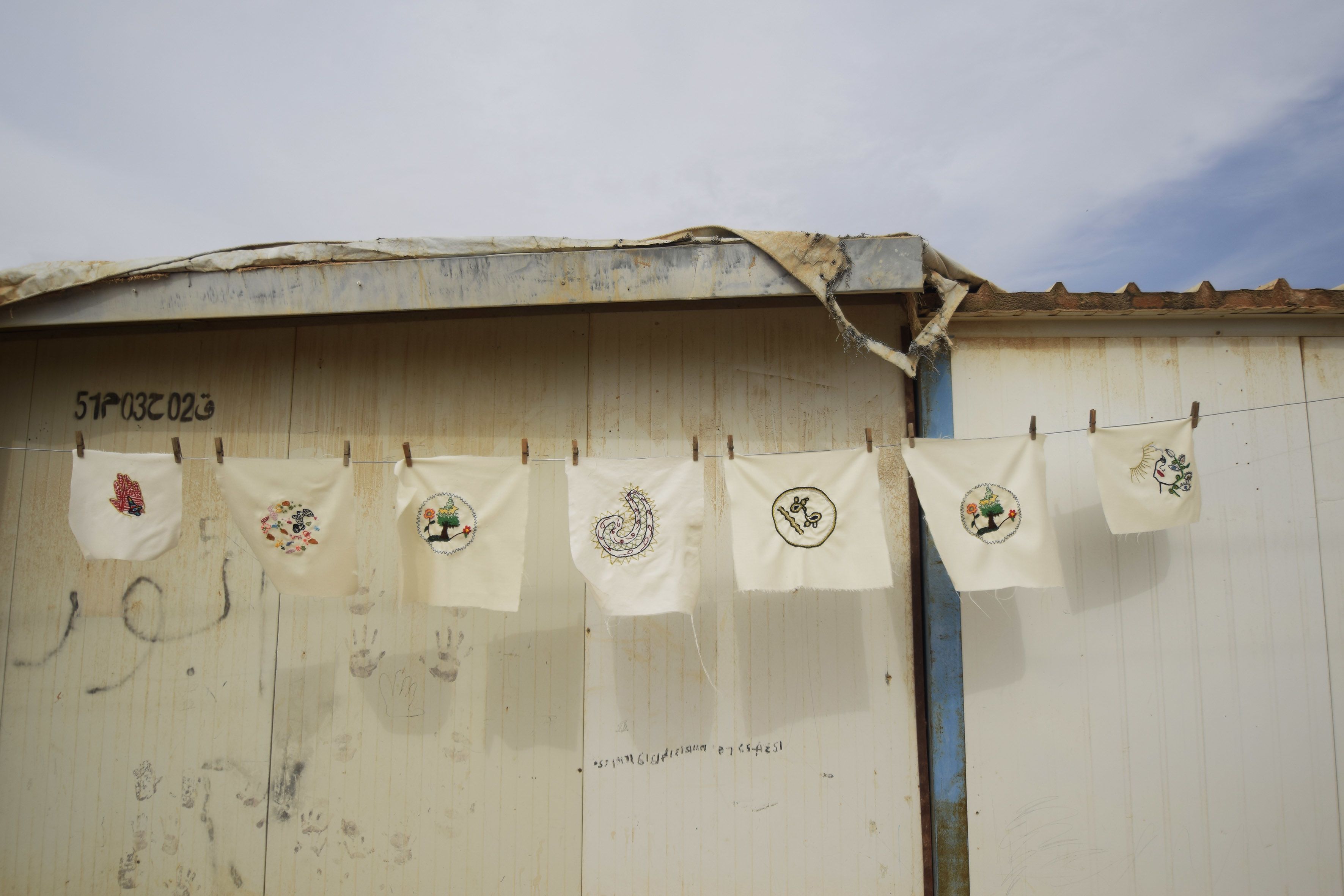 Embroidery samples containing artwork hanging on a line held by pegs 
