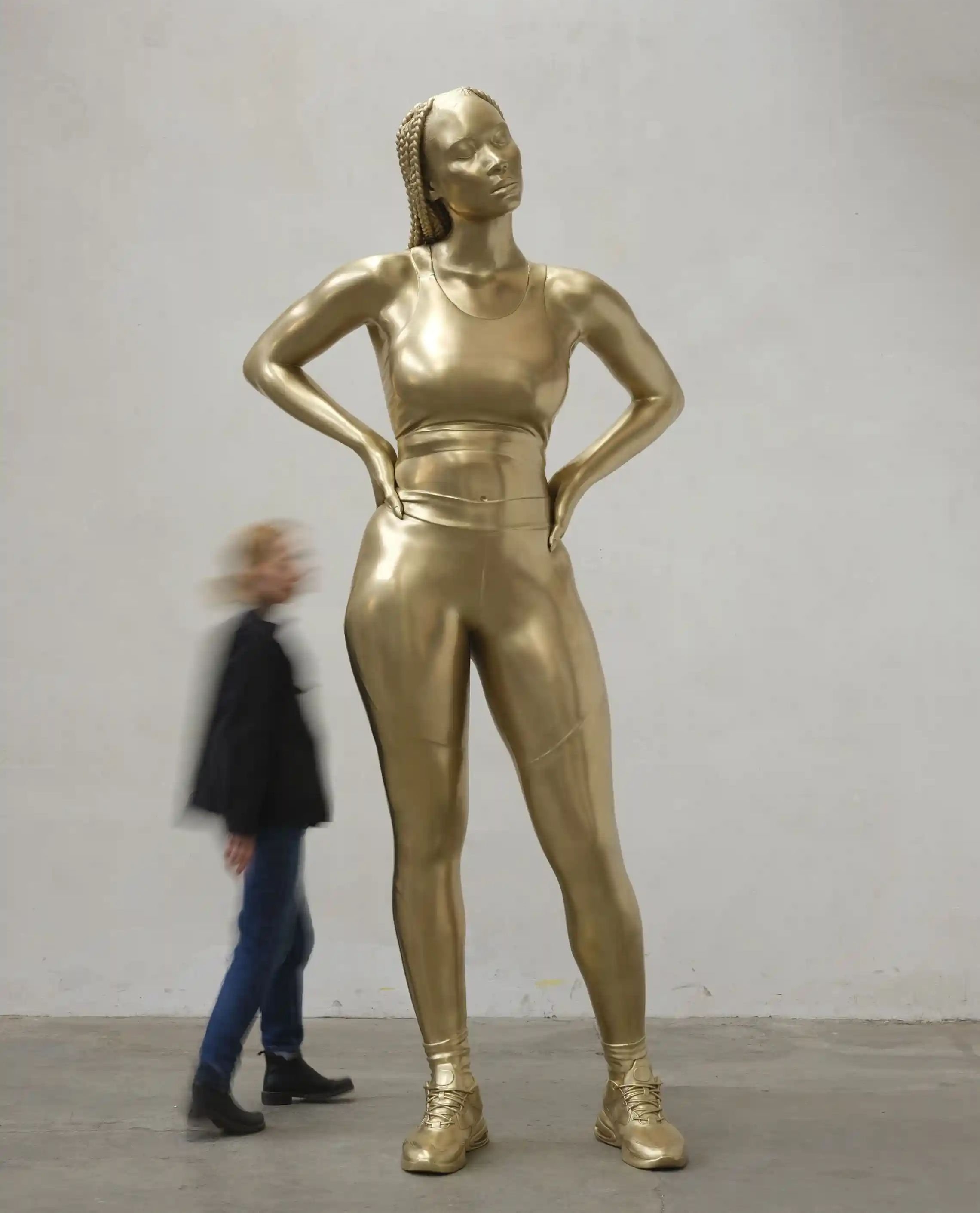 A 2.8m tall sculpture of a young woman in atheisure wear with long braids. She is made of bronze.