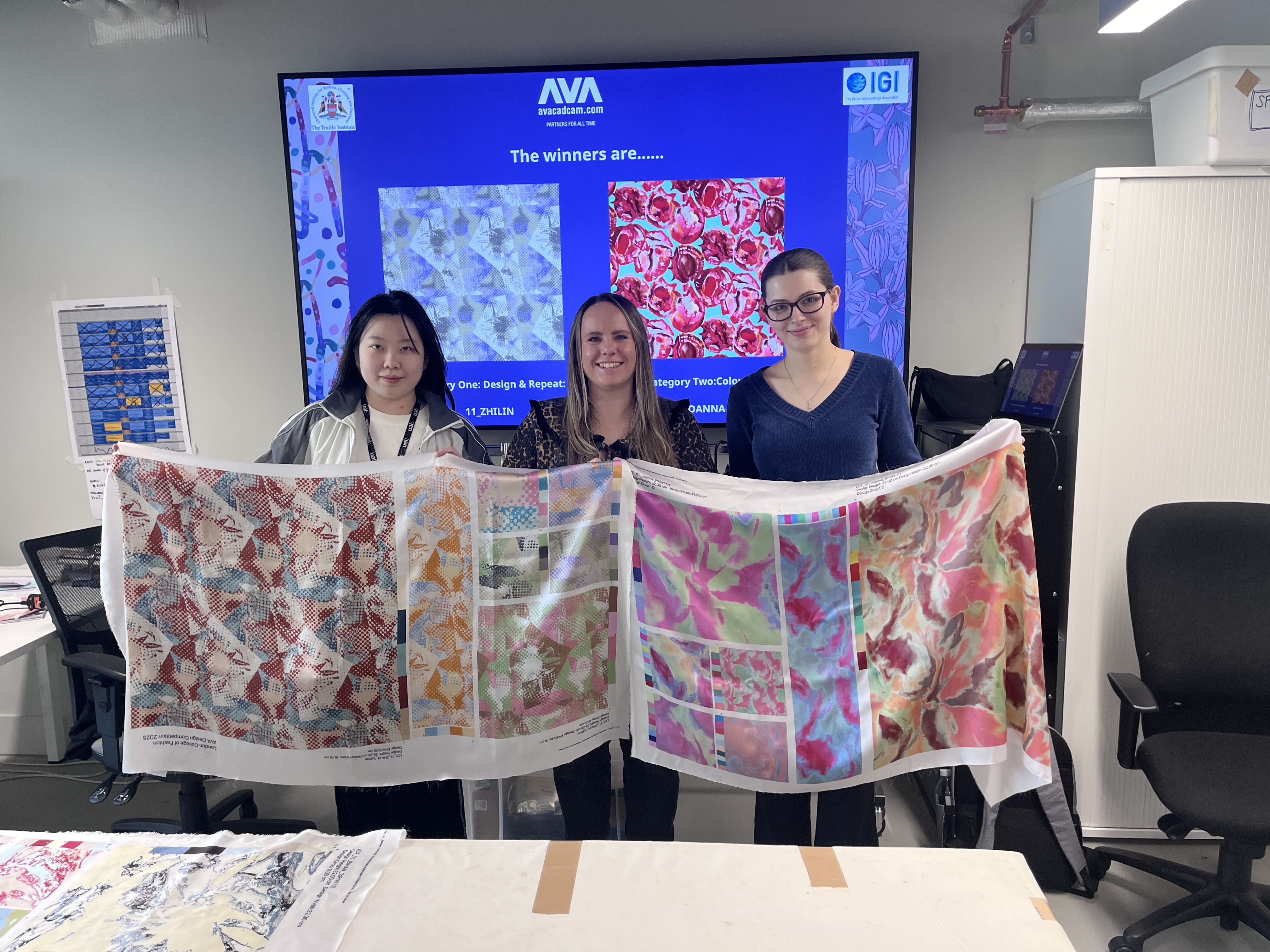 Three people holding up large colourful fabric, smiling at the camera.