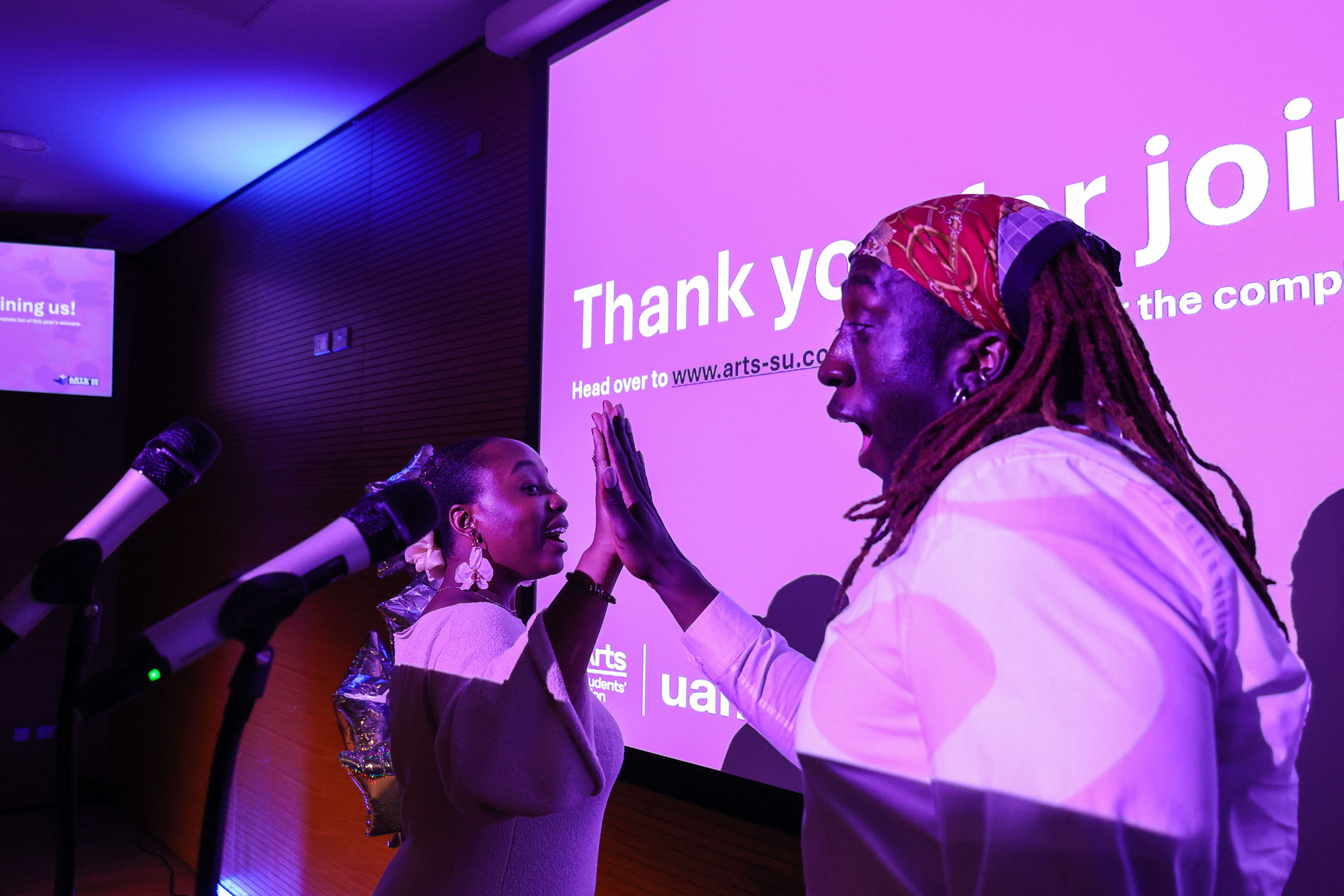 SU Officers Charmiane and Katwamba high five on stage.
