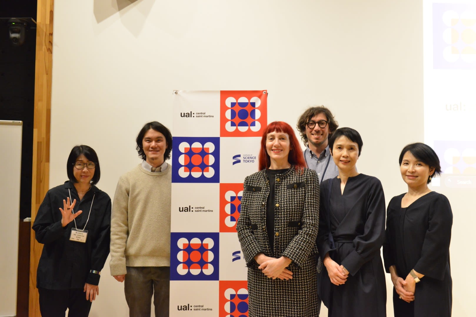 Six people posing in front of a poster featuring blue, orange, black and white university logos.