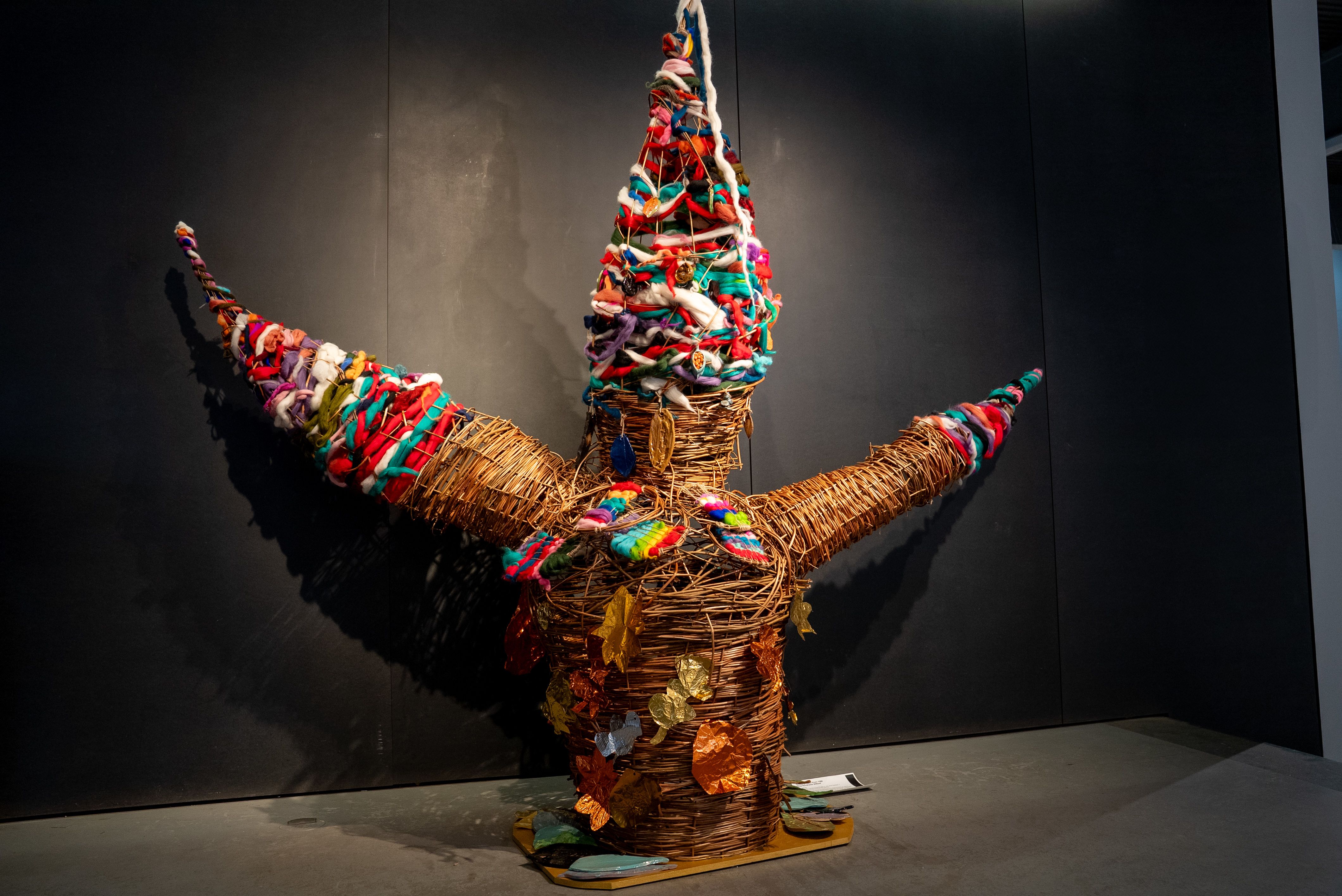 Wooden sculpture with colourful fabrics stitched in and colourful leaves attached.