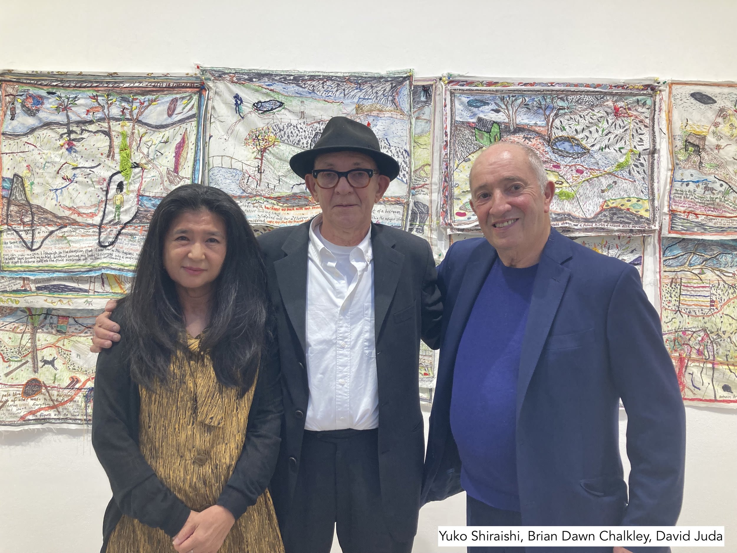 Brian Dawn Chalkley (centre) with Yuko and David Juda. They're stood infront of Brian's work