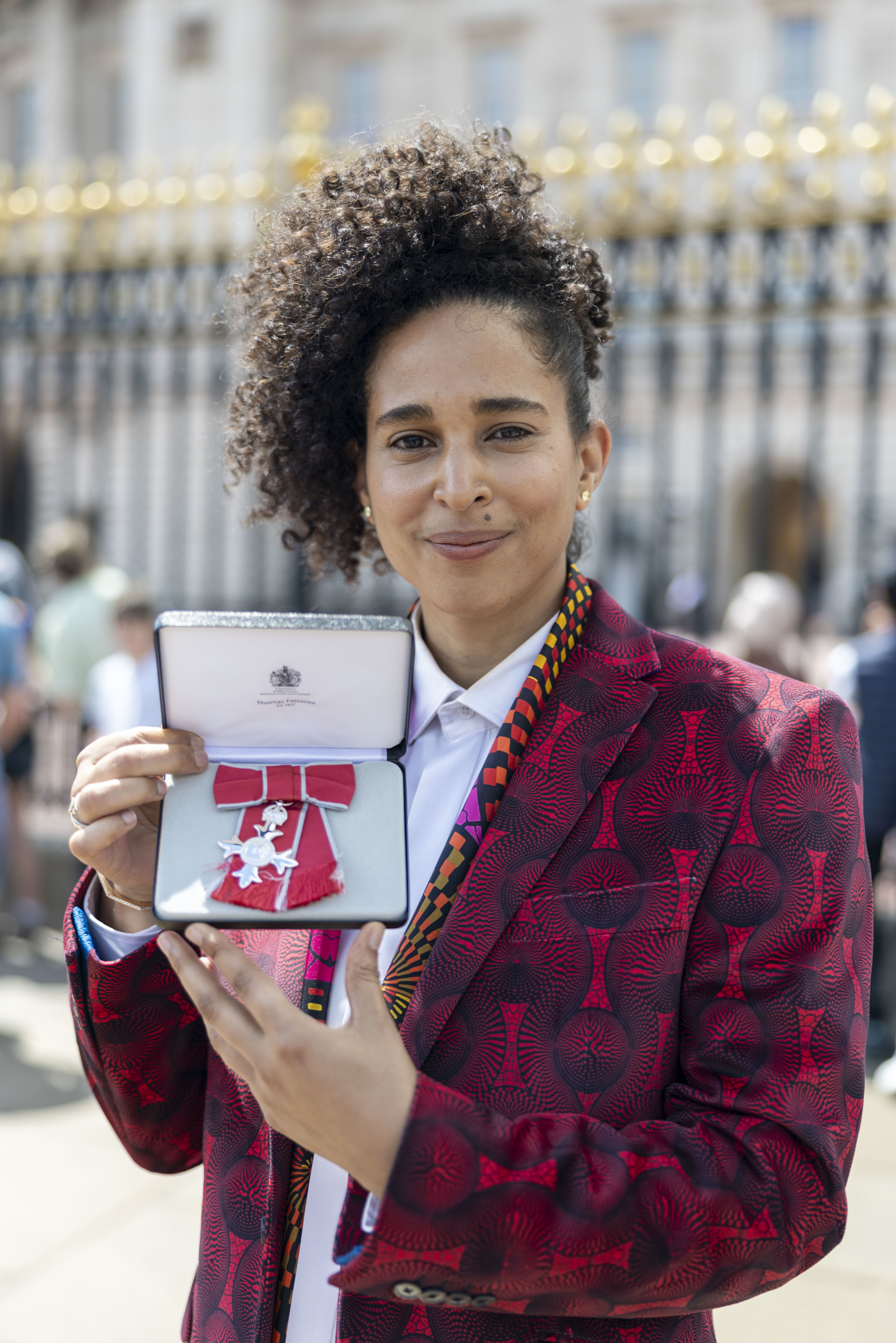 A smiling woman standing infront of Buckingham Palace holding a medal