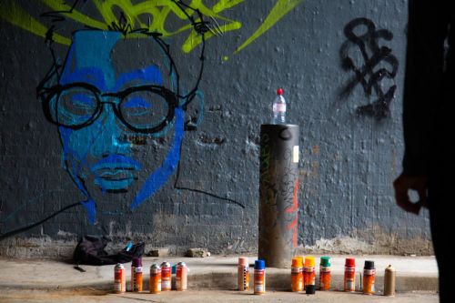 spray paints on the floor in front of a drawn face on wall