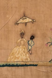 A close-up of a piece of tapestry from the 18th century. It depicts a little figure of a black boy with an adult in rich dress under a parasol